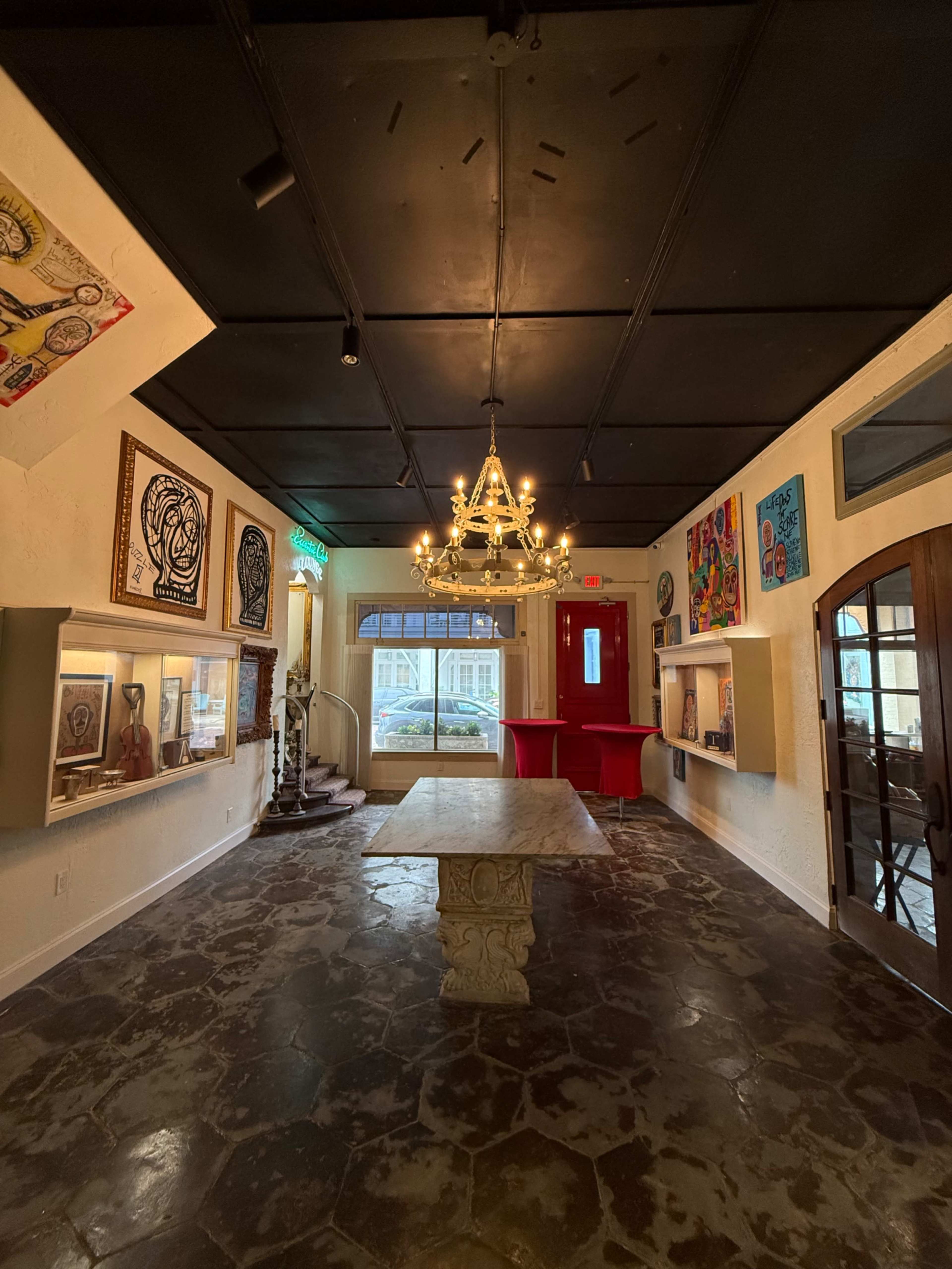 The image shows an art gallery with stone flooring, a central table, and illuminated artworks lining the walls.