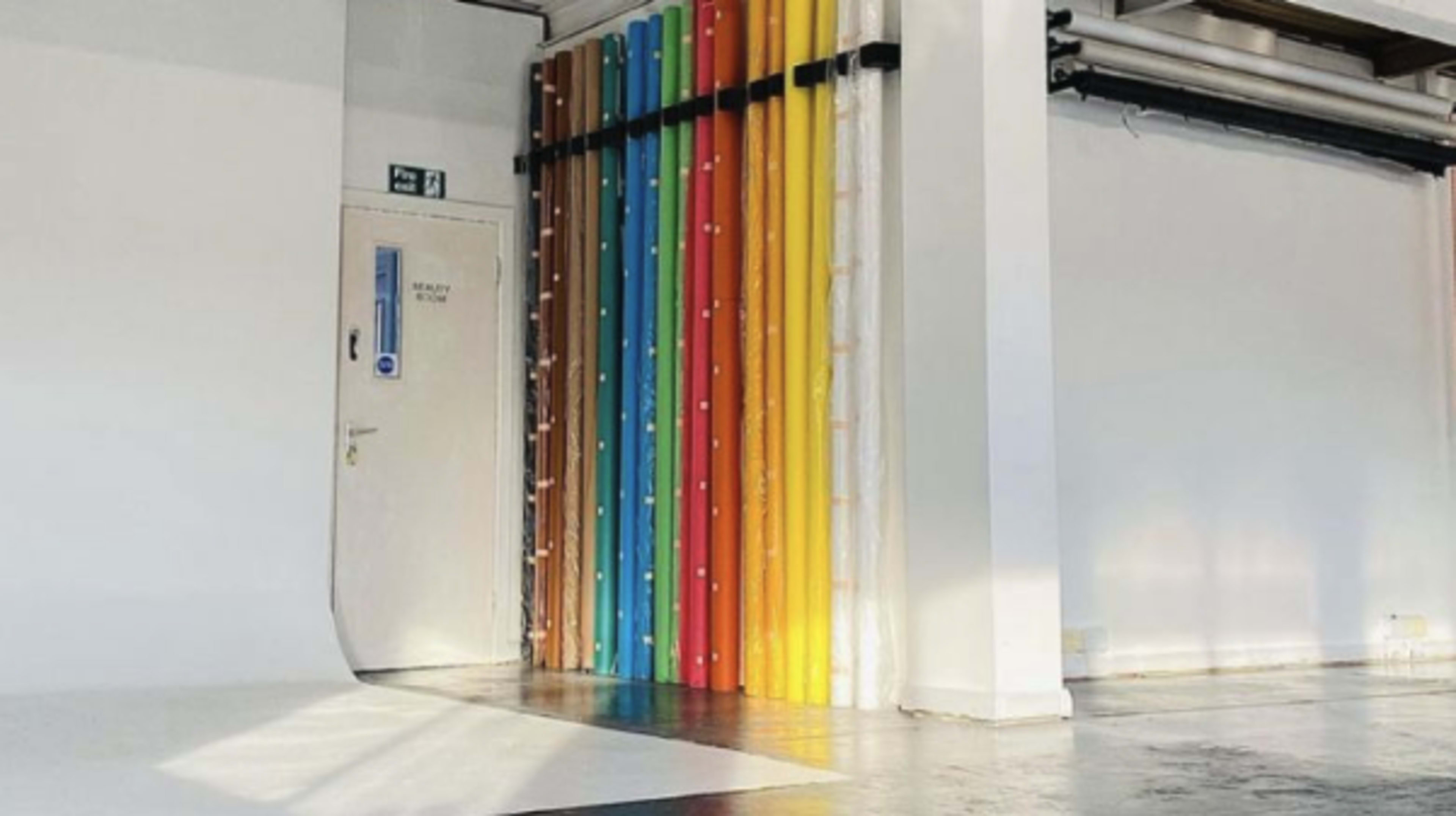 A bright, minimalist interior space featuring a door and a wall adorned with colorful rolled materials.
