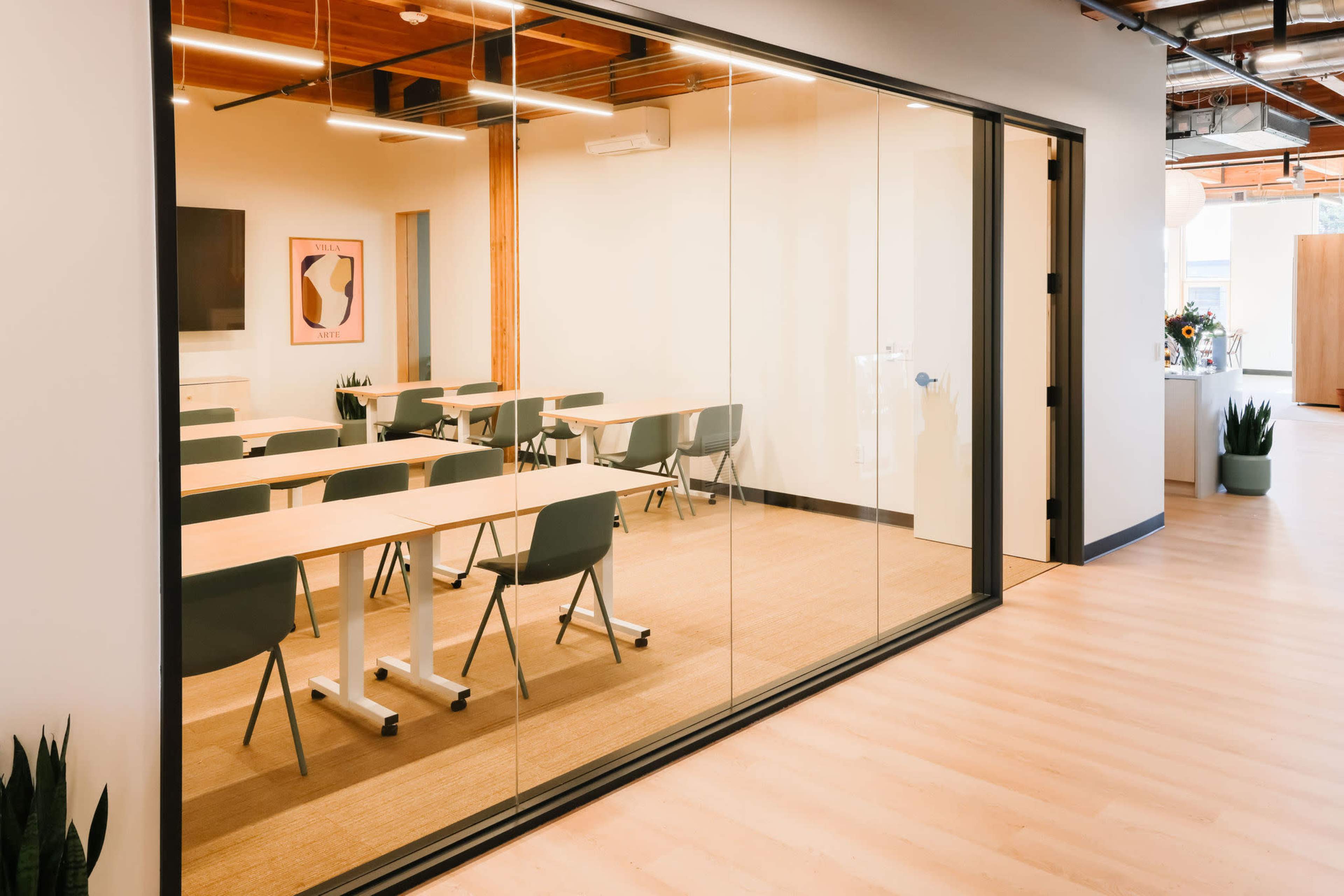 The image shows a glass-walled conference room with rows of empty tables and chairs arranged inside.