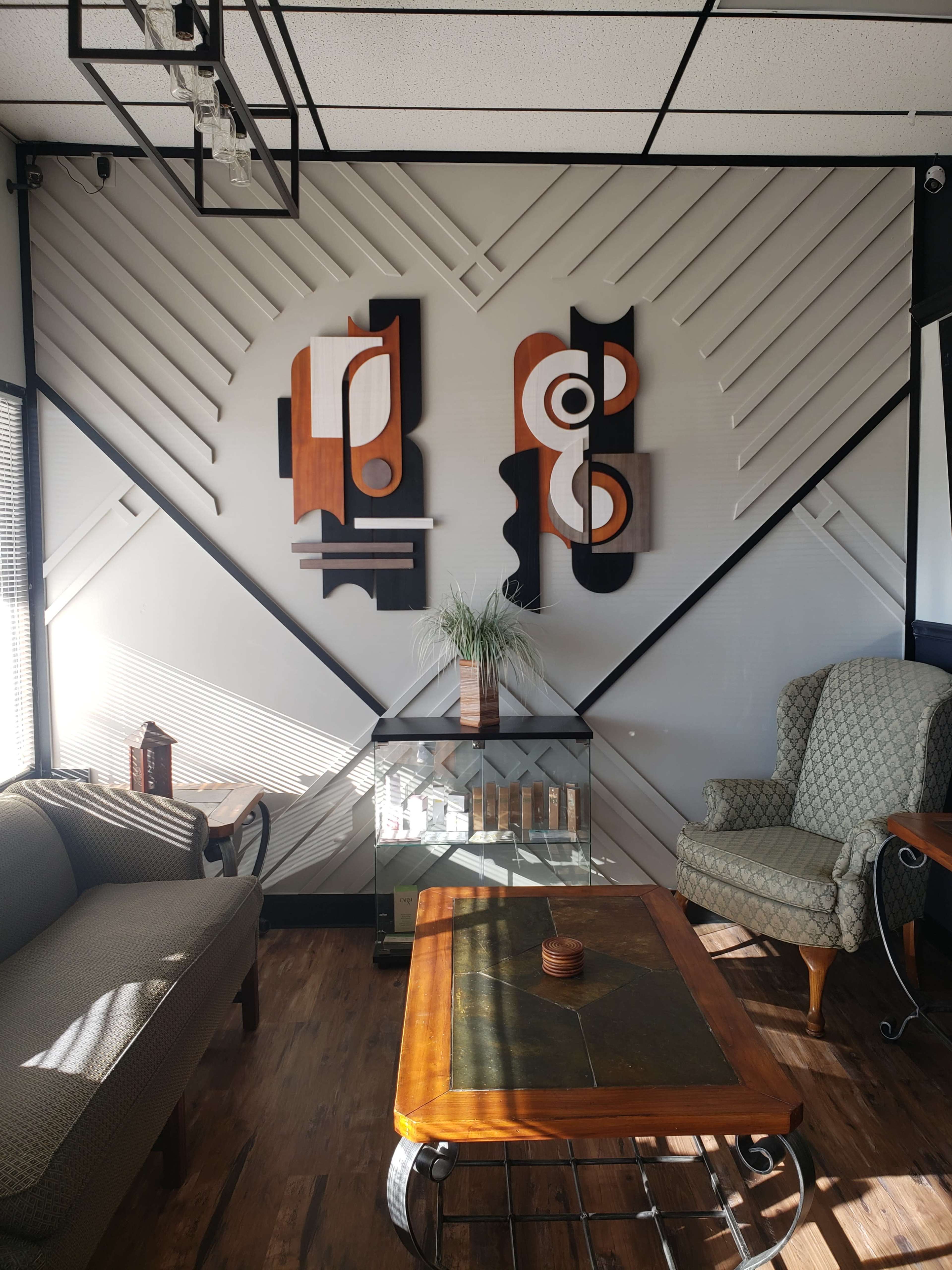 The image shows a modern living area with two abstract wall art pieces, a glass coffee table, and a patterned armchair.