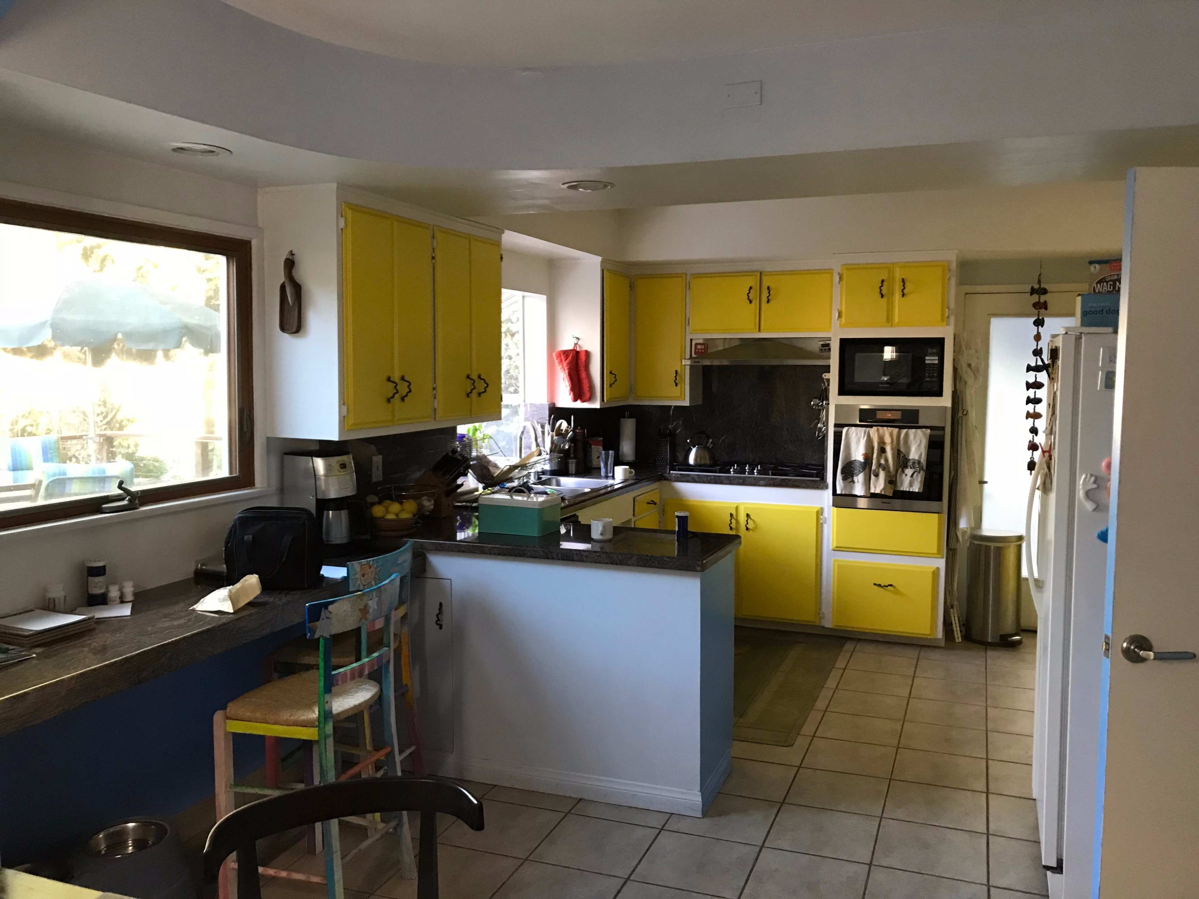 A kitchen with yellow cabinets, a black countertop, and a window overlooking an outdoor space.
