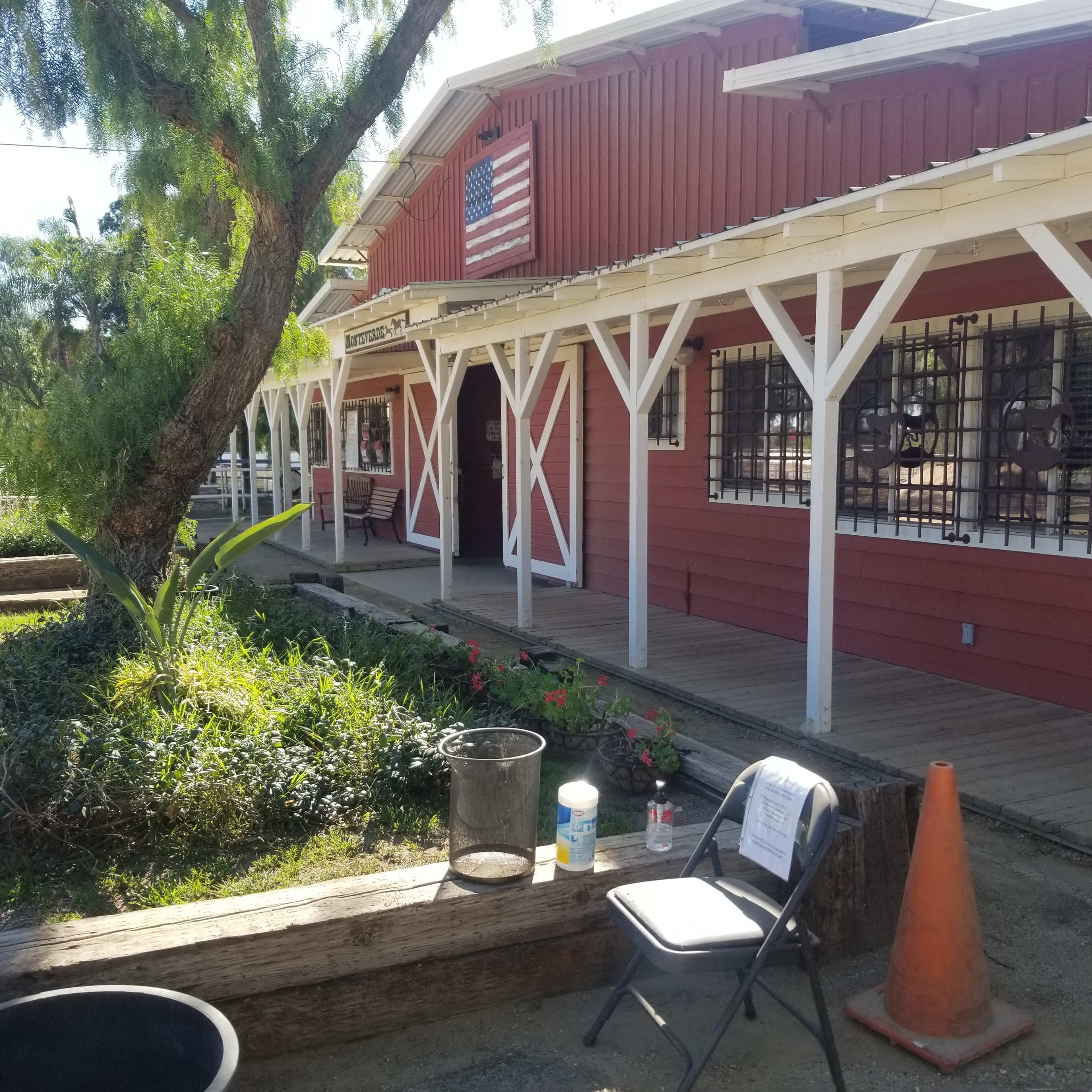A red wooden building with an American flag, surrounded by greenery and a wooden bench in front.