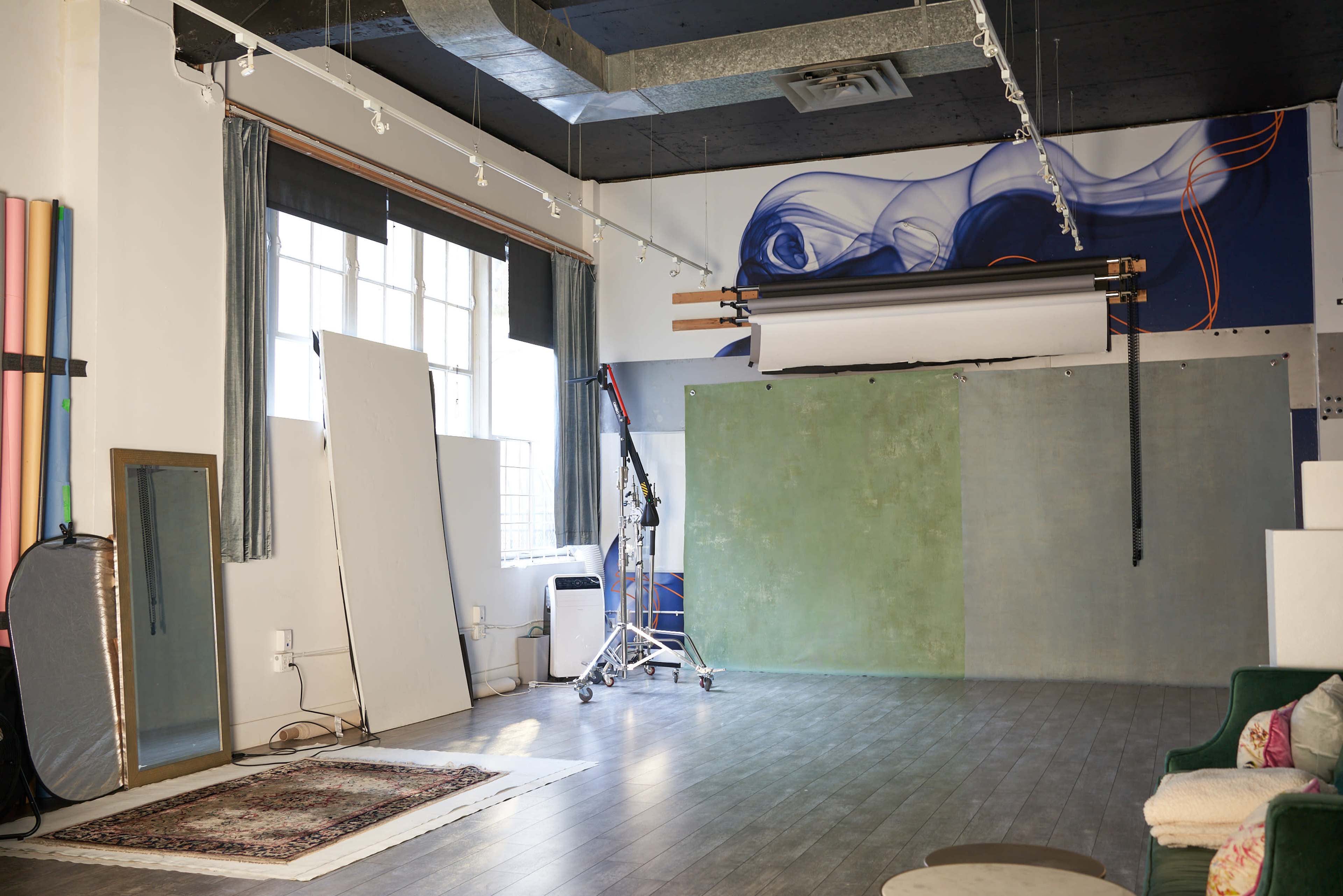 The image shows a photography studio with a large backdrop setup, a mirror, props, and a patterned rug on the floor.