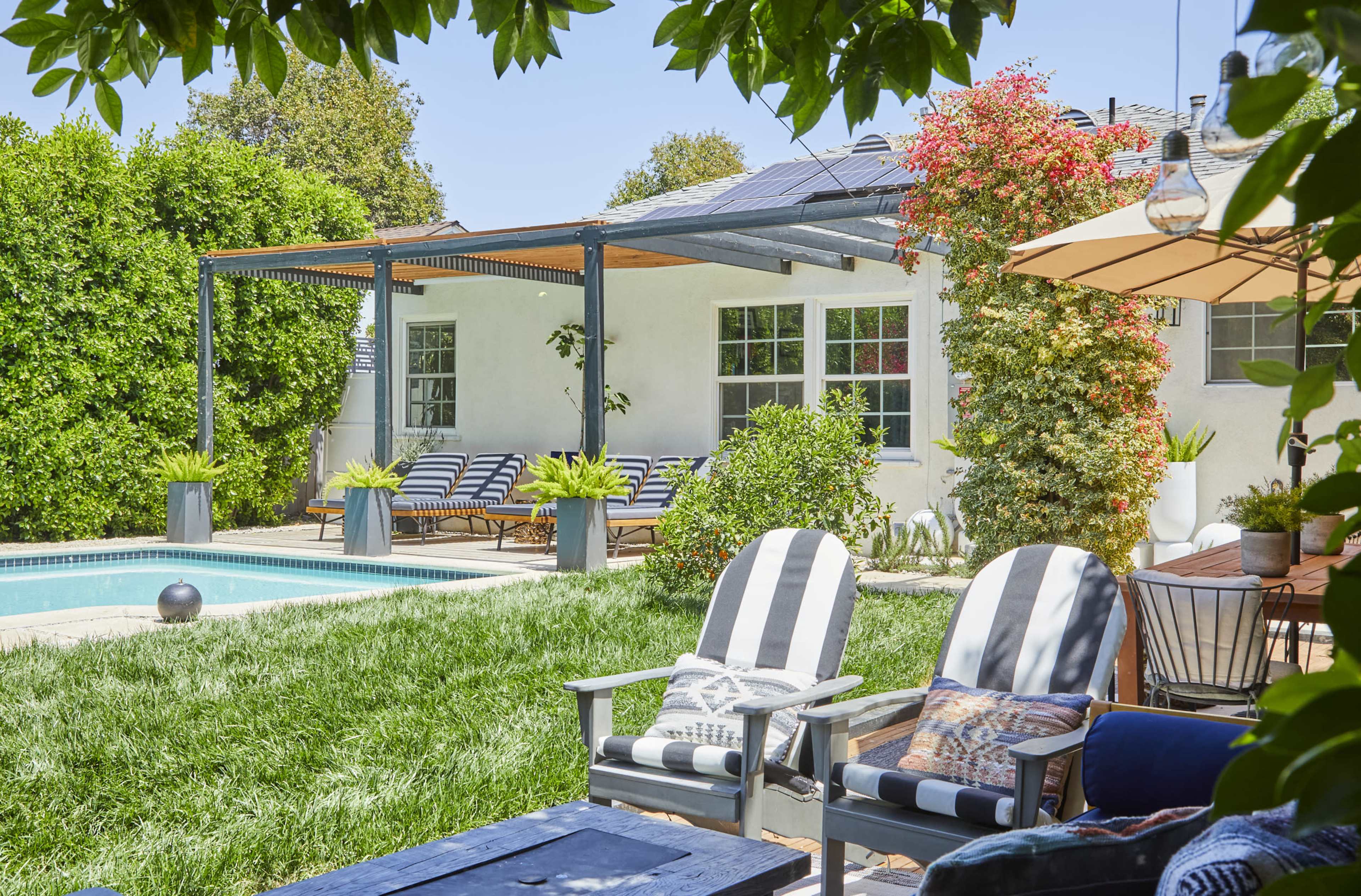 A backyard with a swimming pool, patio furniture, and lush greenery surrounding a white house.