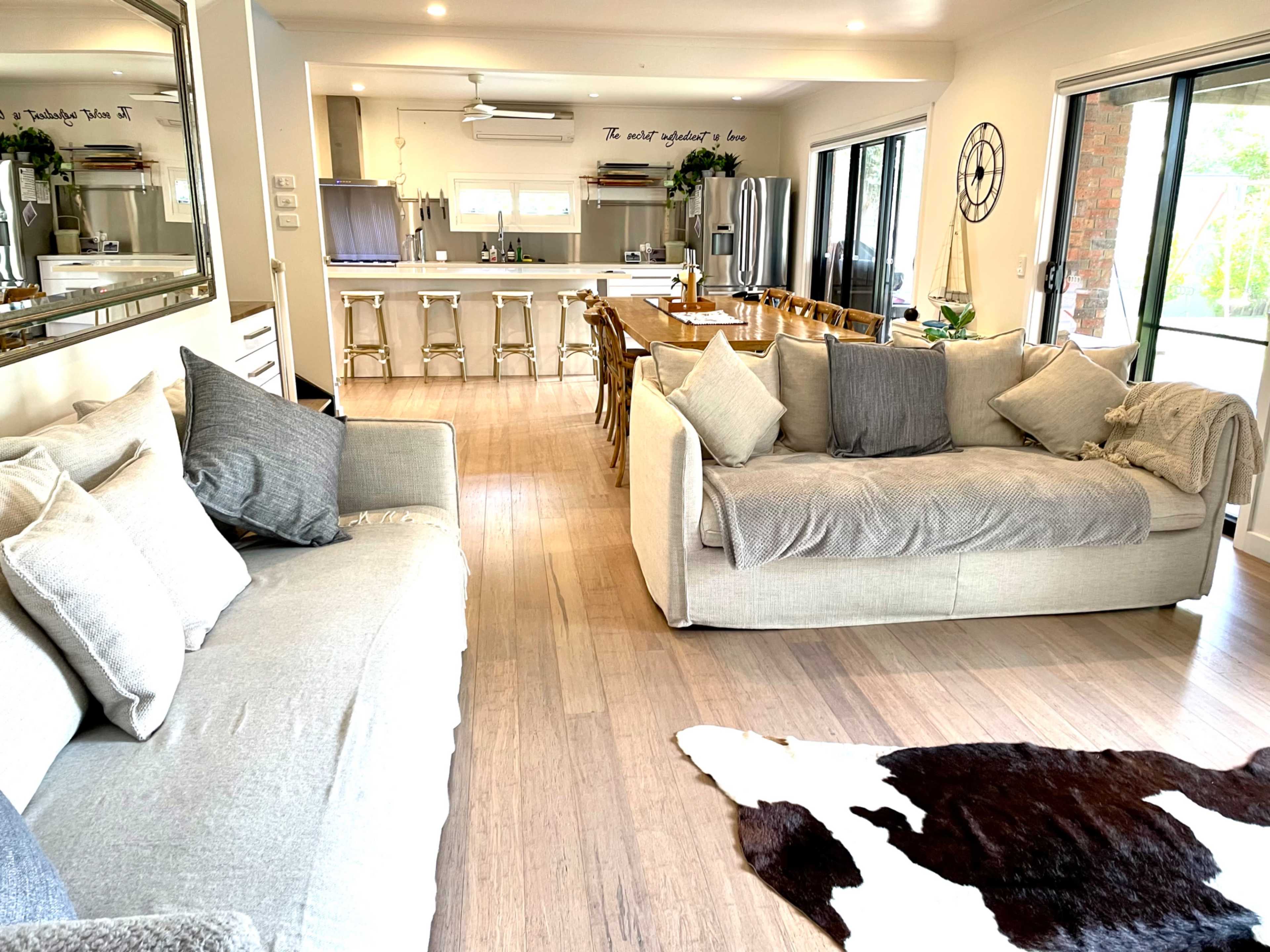 A spacious, modern living area featuring two sofas, a dining table, and a well-equipped kitchen in the background.