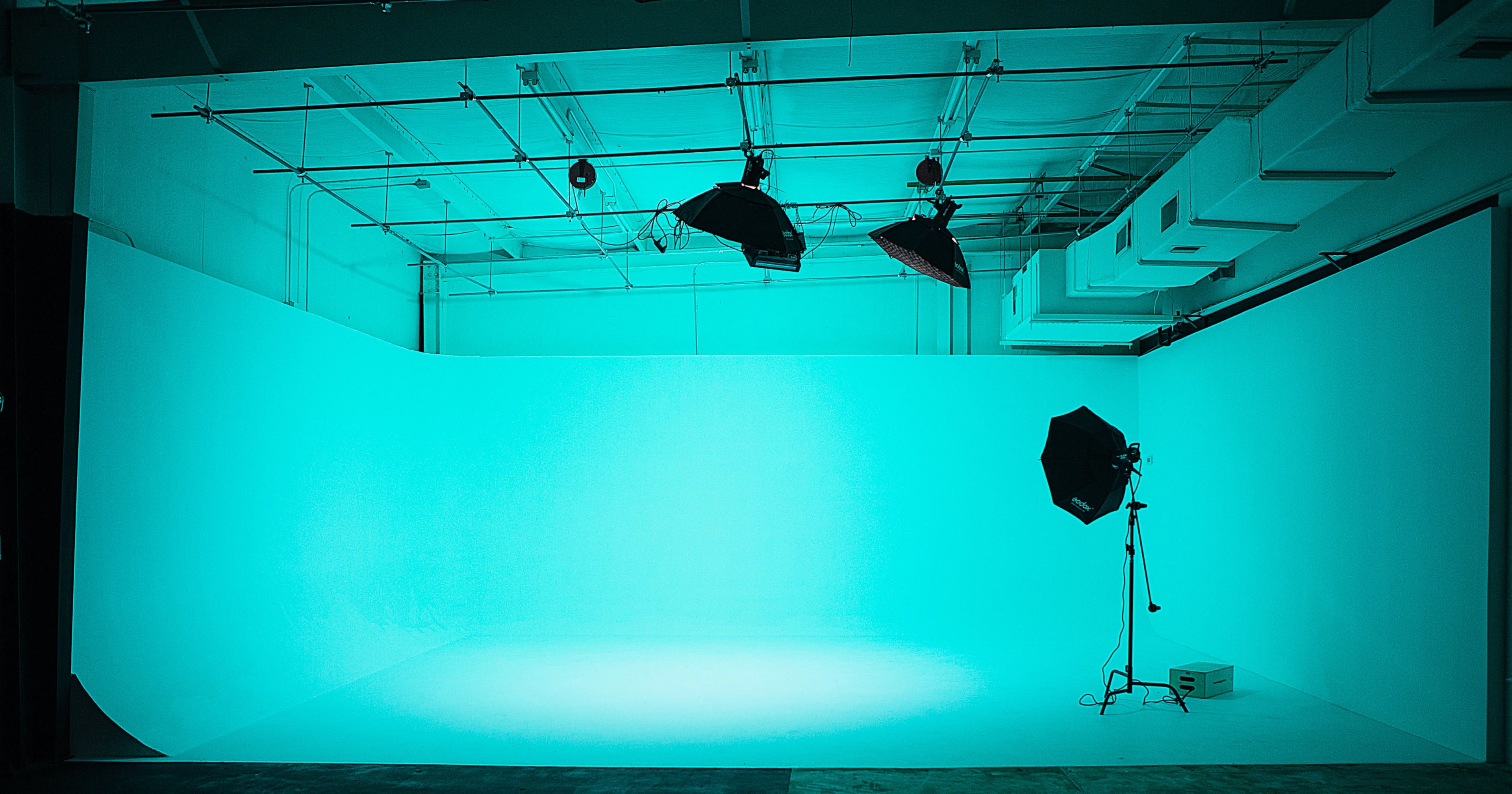 A photography studio with a plain turquoise backdrop and lighting equipment set up.