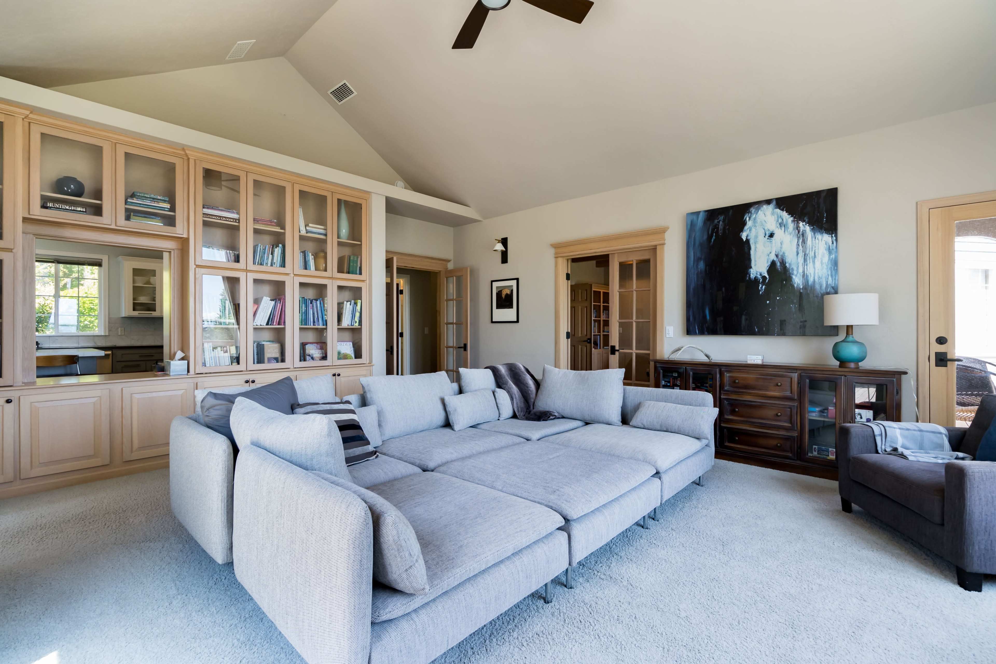 A spacious living room featuring a large sectional sofa, built-in bookshelves, and a wooden side table with a lamp.