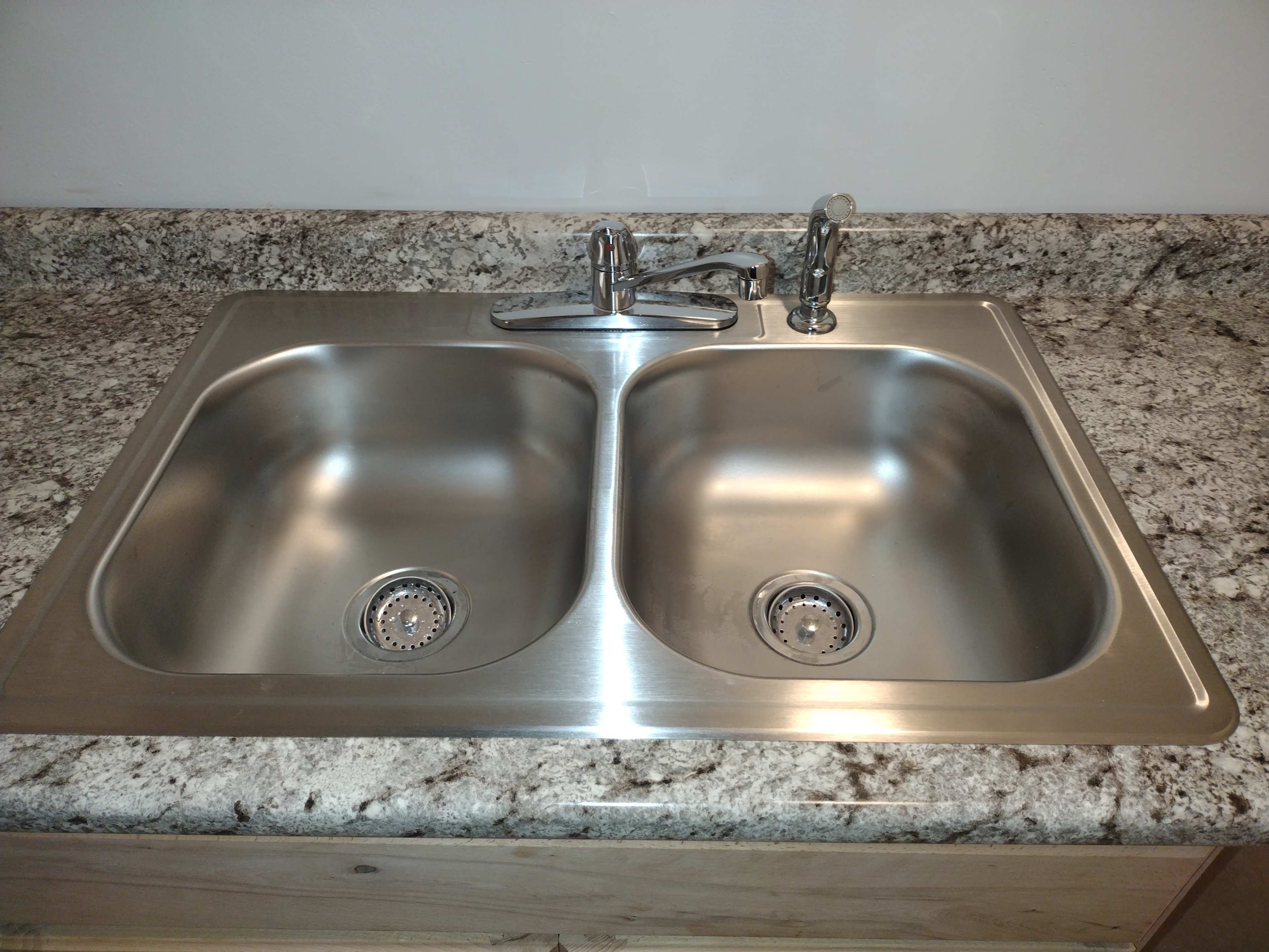 A stainless steel double sink installed on a speckled granite countertop.