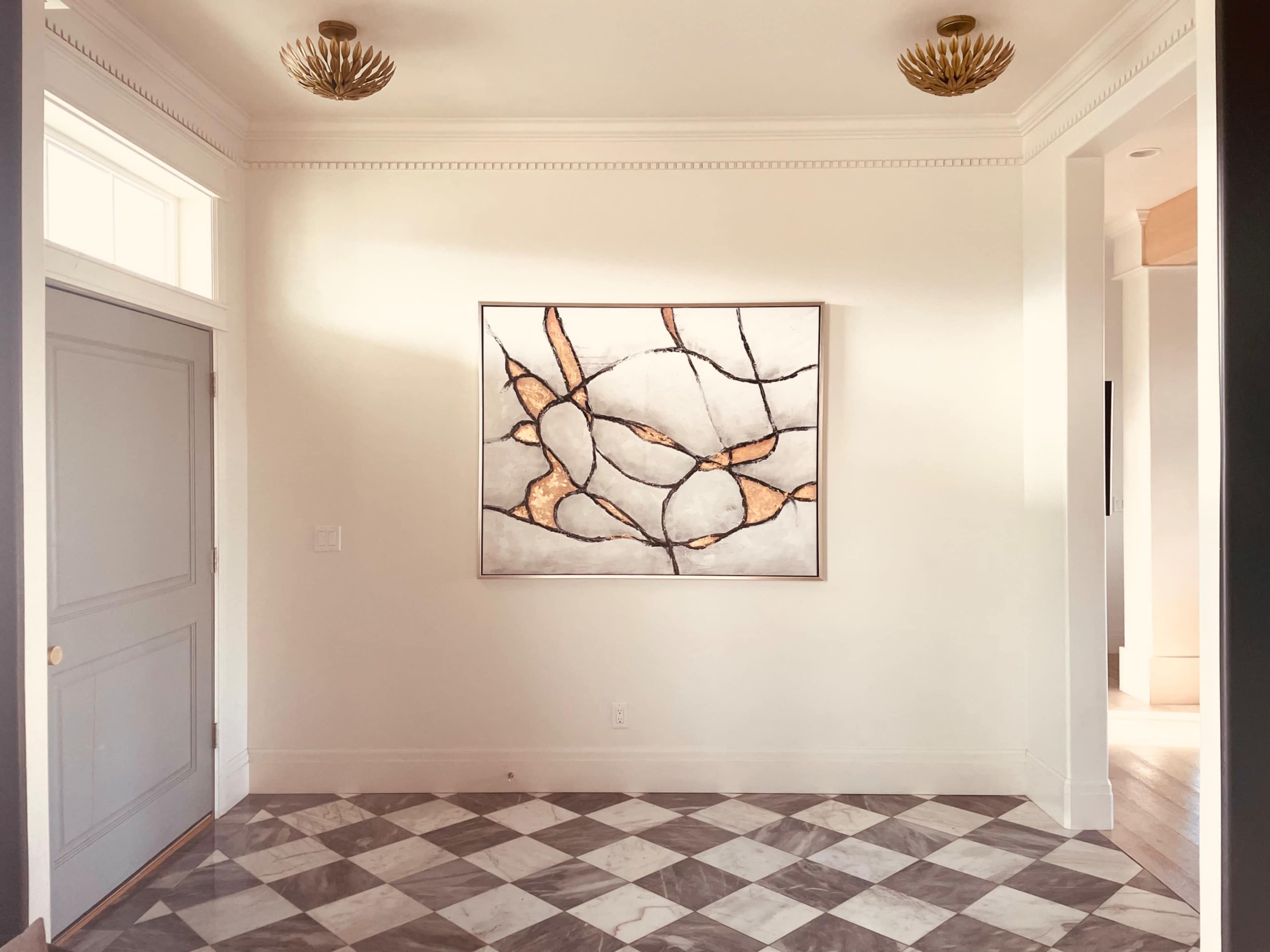 A spacious entryway with a geometric art piece mounted on a light-colored wall above a checkered floor.