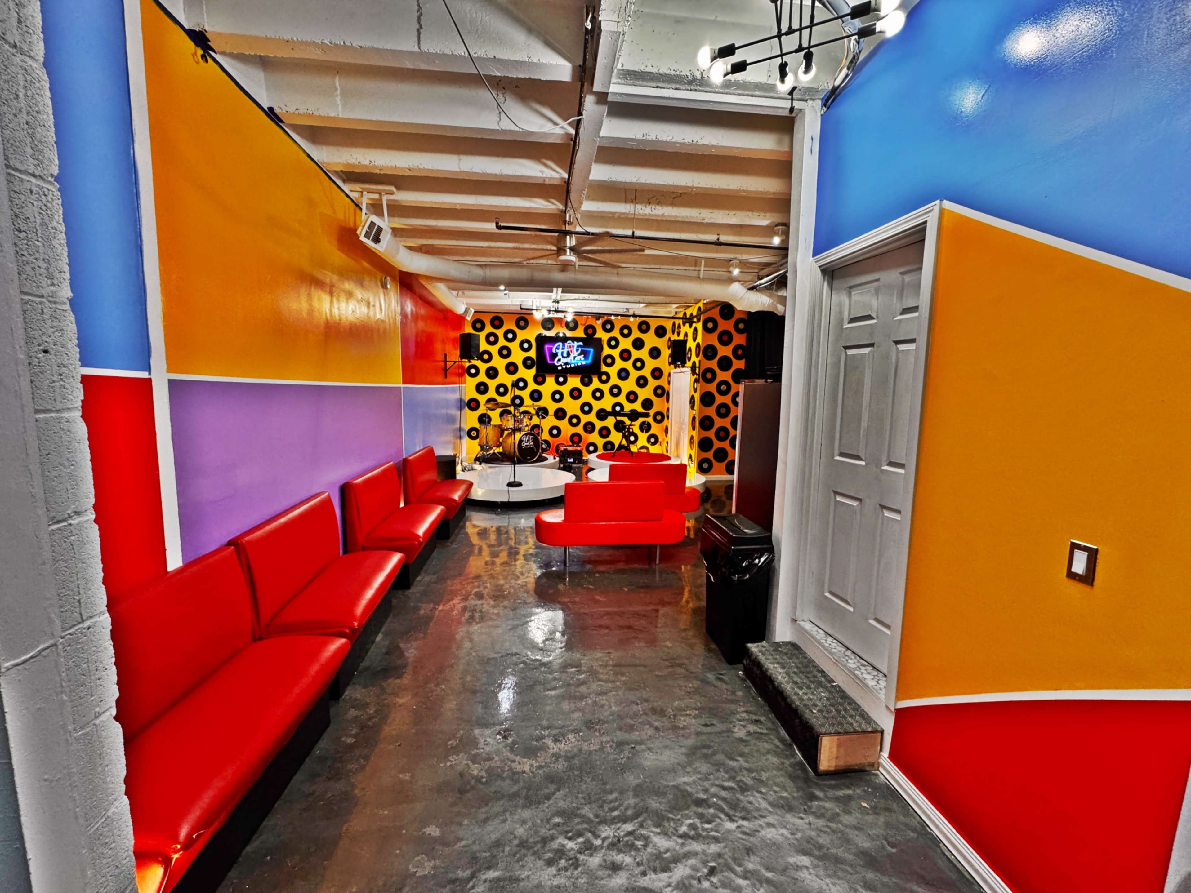 A brightly colored interior features red seating along one side and a circular stage area with a patterned backdrop at the far end.