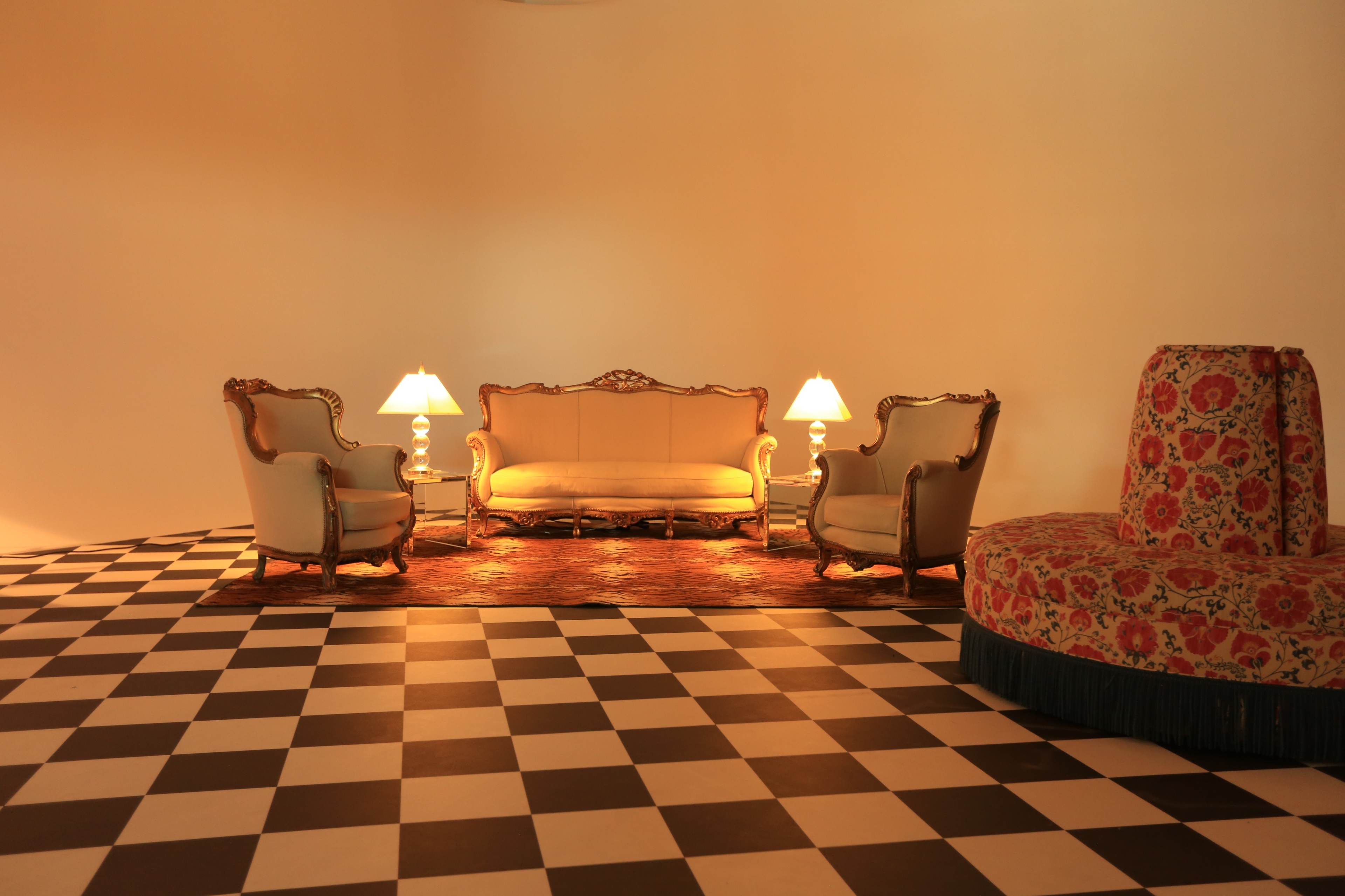 The image shows a sitting area with two armchairs and a sofa, accompanied by two lamps, arranged on a checkered black and white floor.