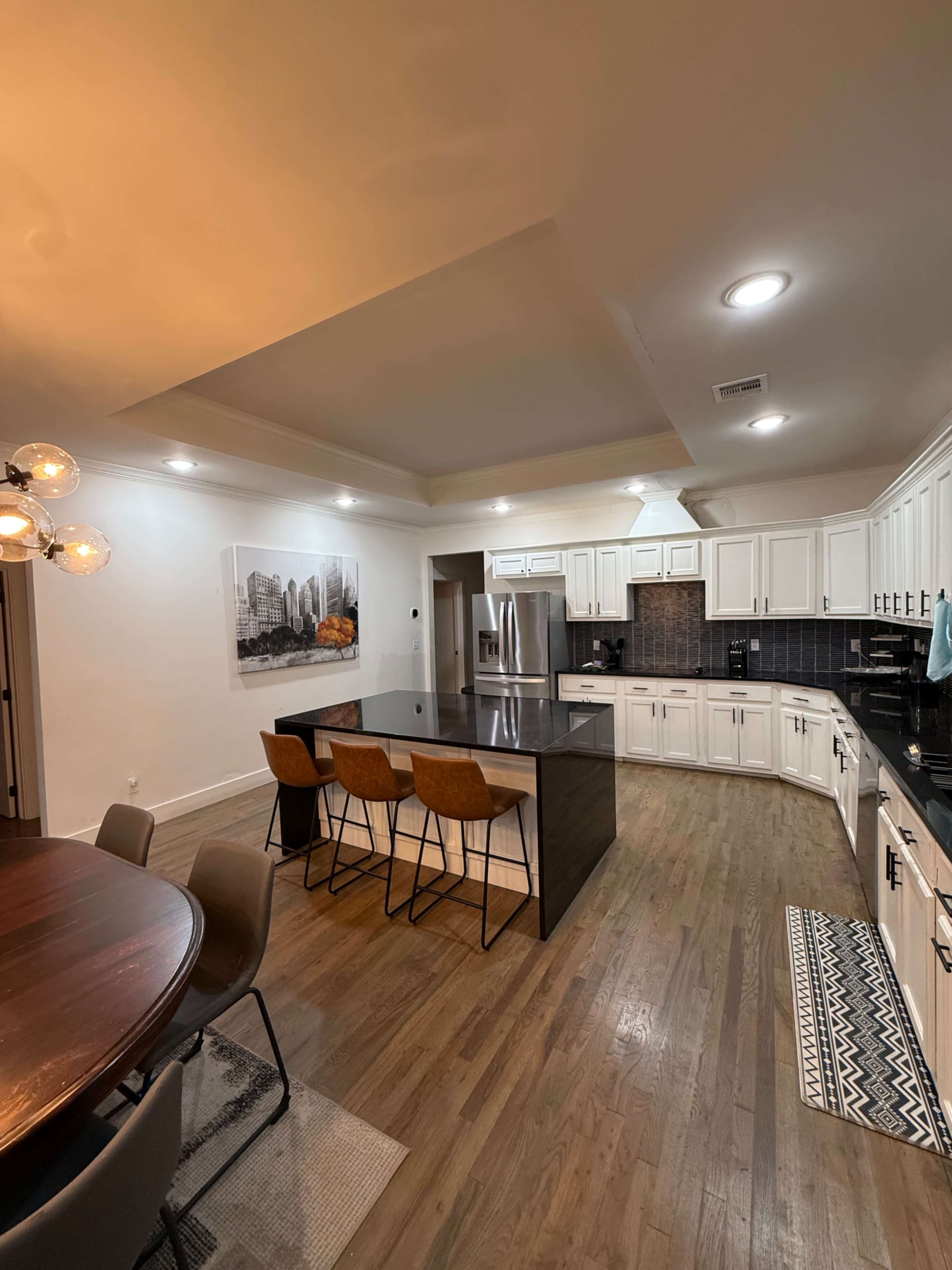 The kitchen features white cabinets, a large island with seating, and modern appliances, alongside a dining area with a round table.