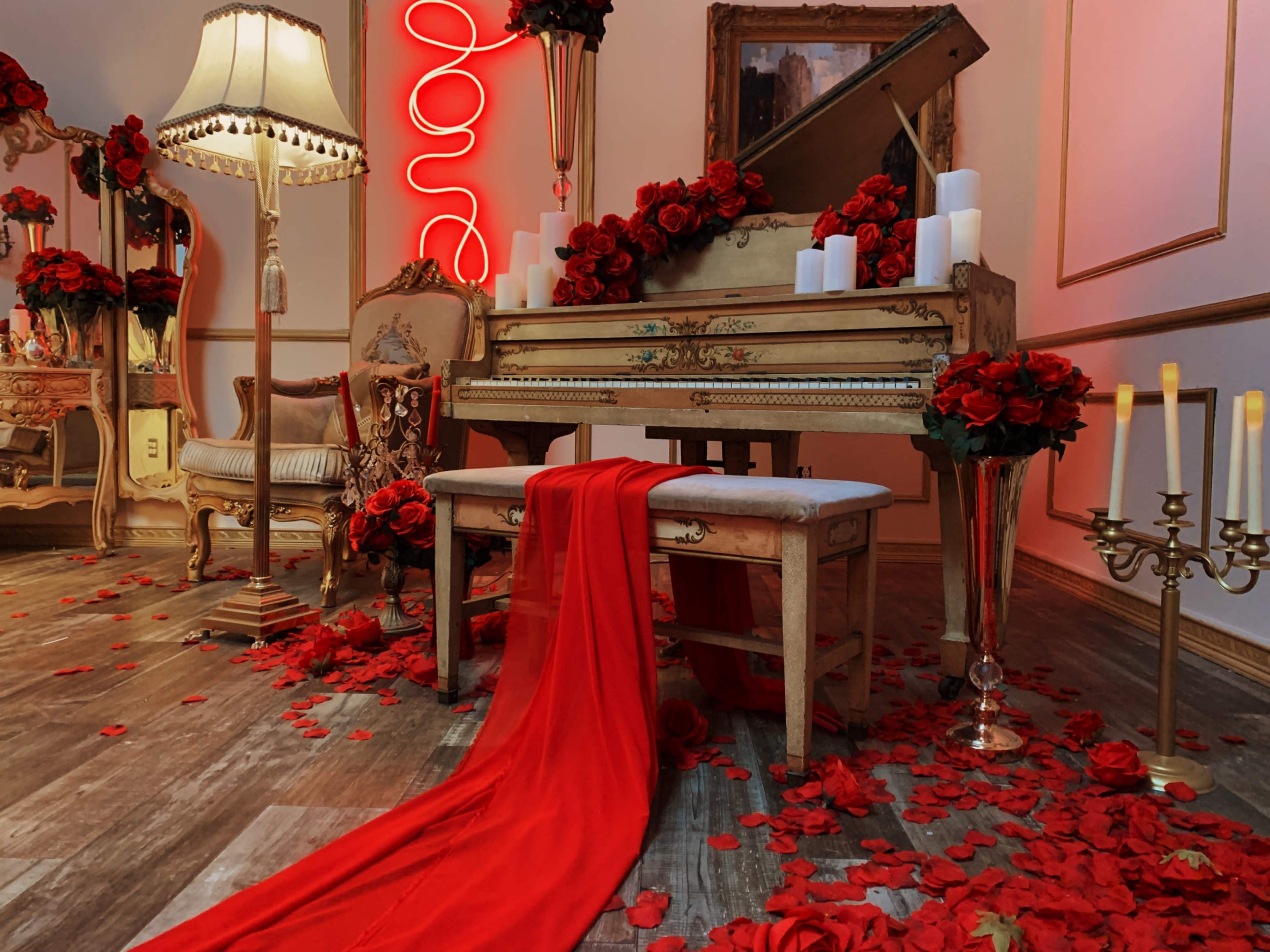 A vintage piano adorned with red roses and candles is set against a backdrop of elegant furnishings and soft lighting.