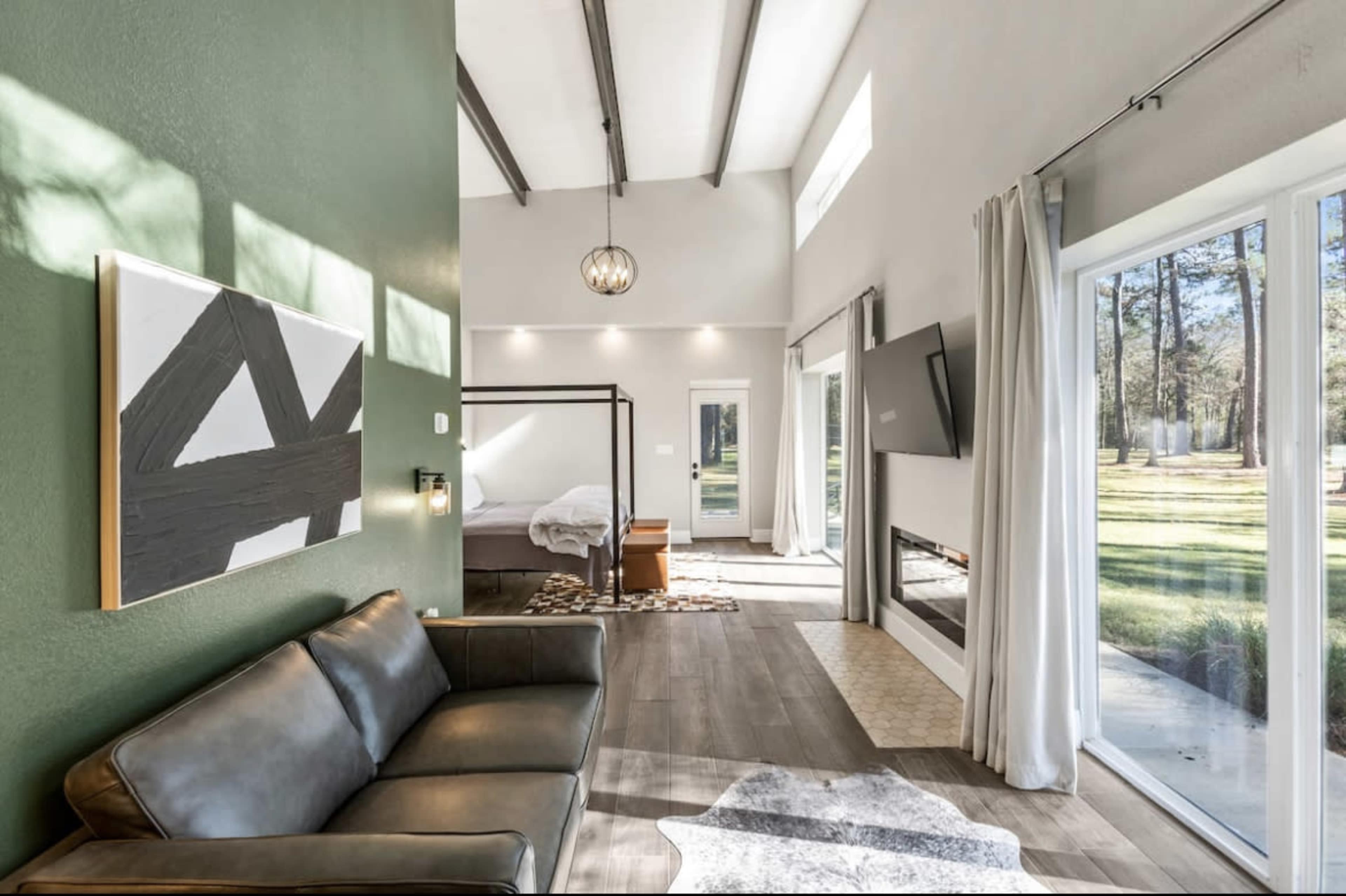 A modern living space with a green accent wall, a leather sofa, a bed in the background, and large windows that open to a scenic outdoor view.
