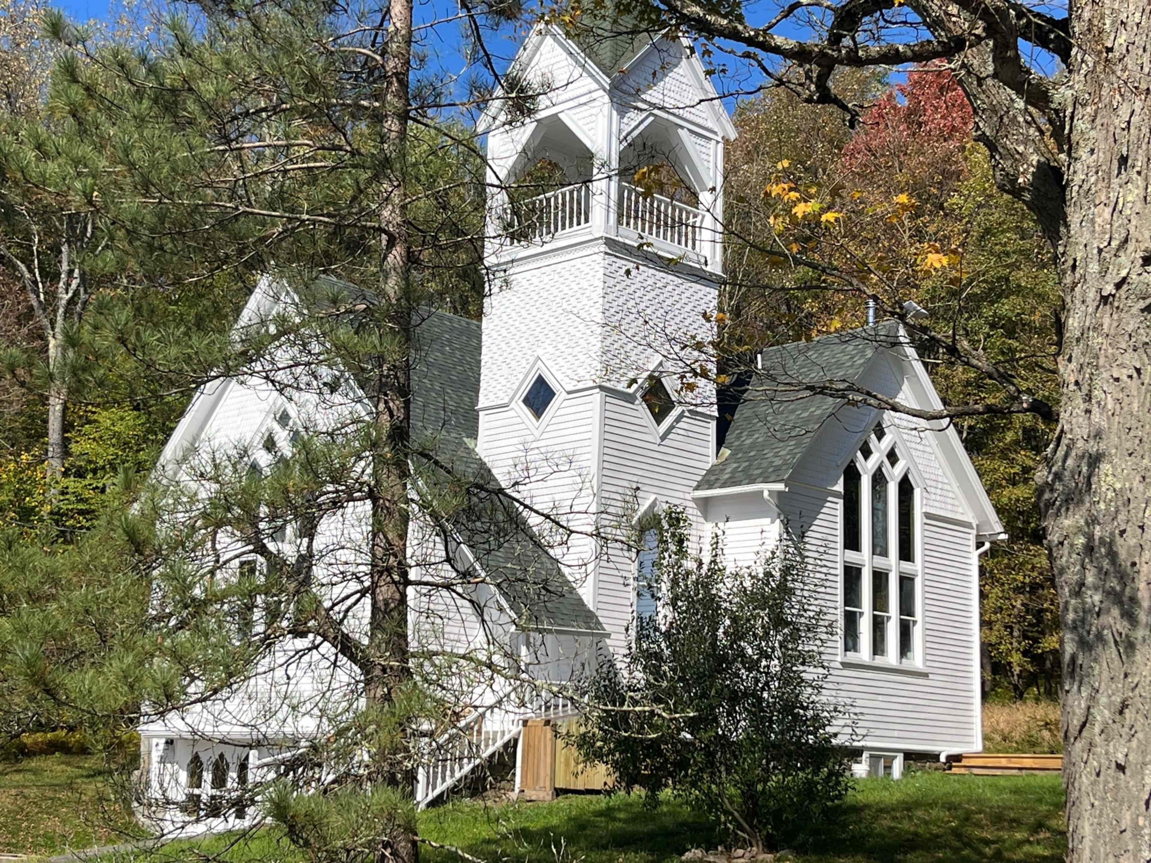 A white church with a bell tower stands amidst trees and autumn foliage.