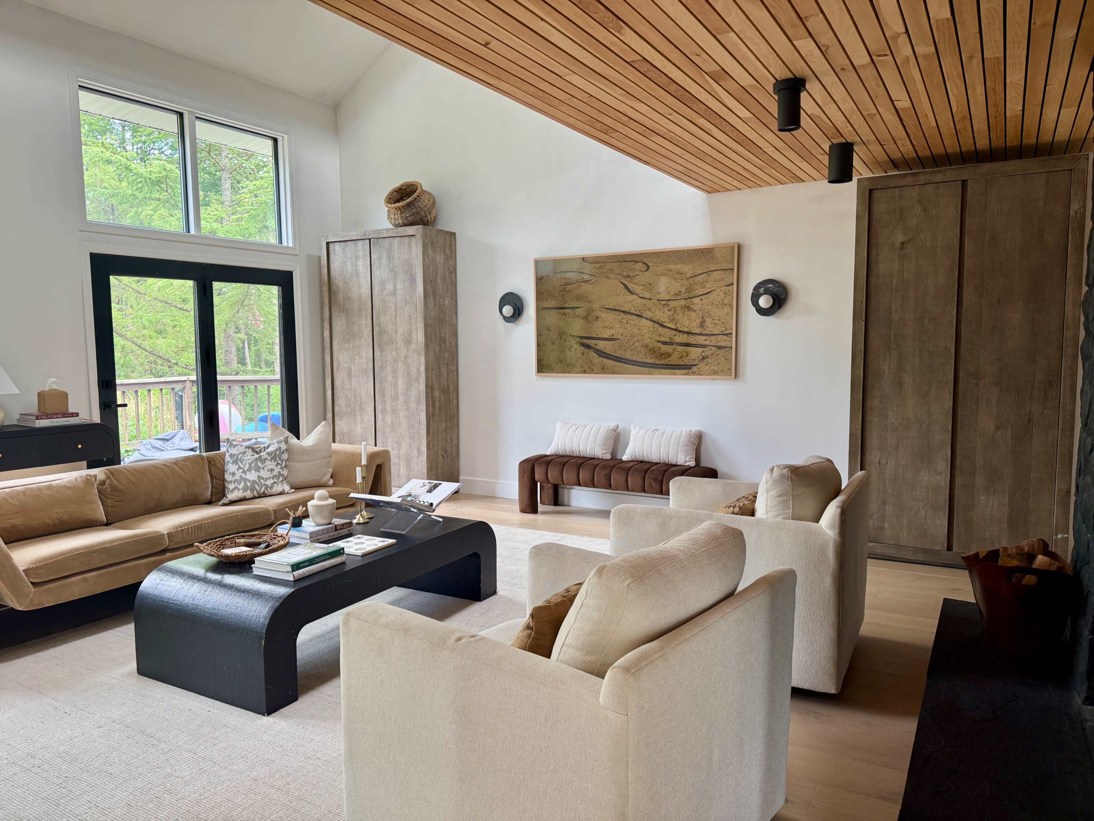 The room features a bright, modern living area with wooden accents, a large coffee table, and comfortable seating arranged around a central focal point.