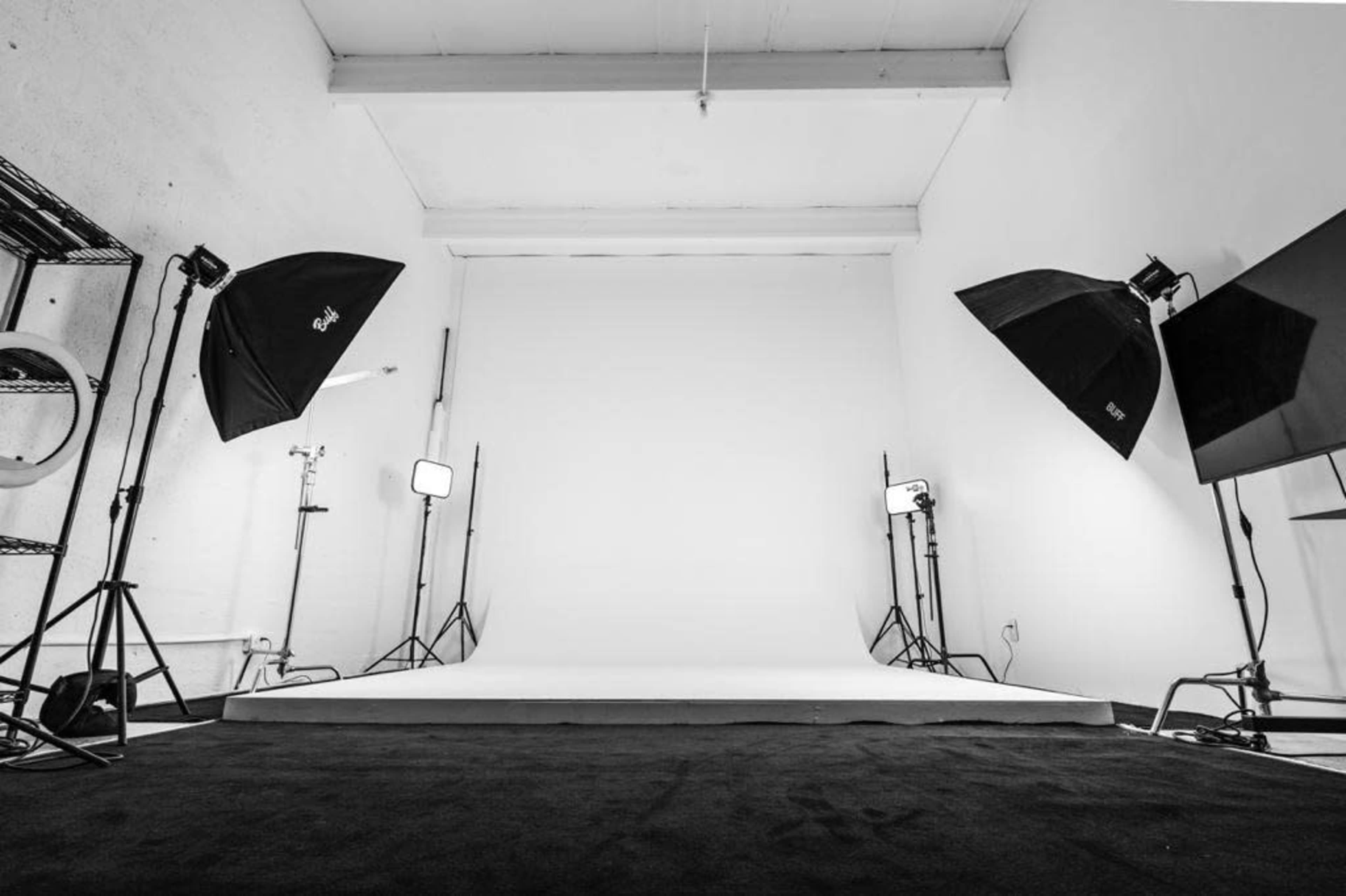 A photography studio features a blank backdrop surrounded by multiple lighting setups and a dark carpet.