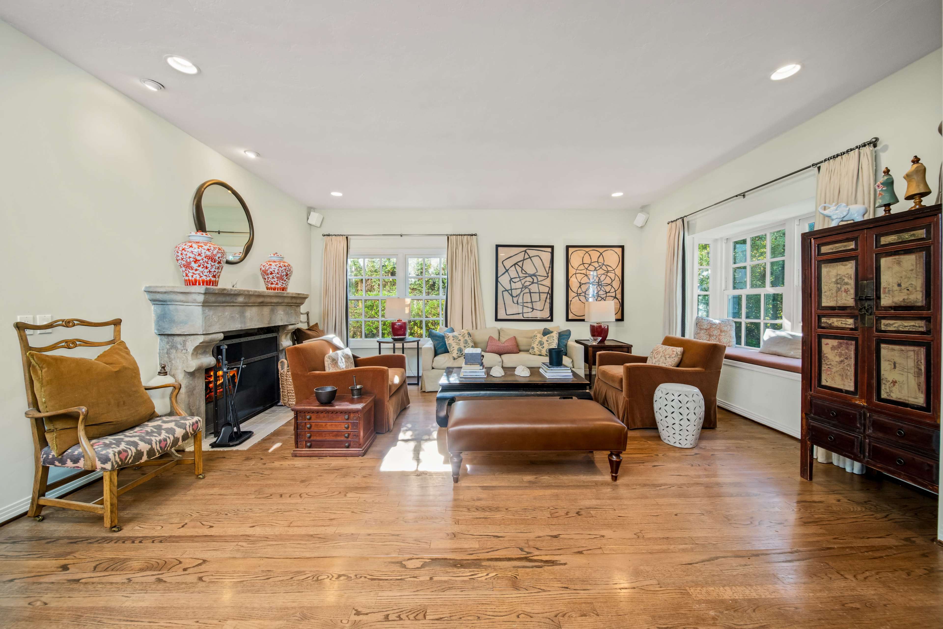 The room features a spacious living area with wooden floors, a stone fireplace, comfortable seating arrangements, and decorative accents against light-colored walls.