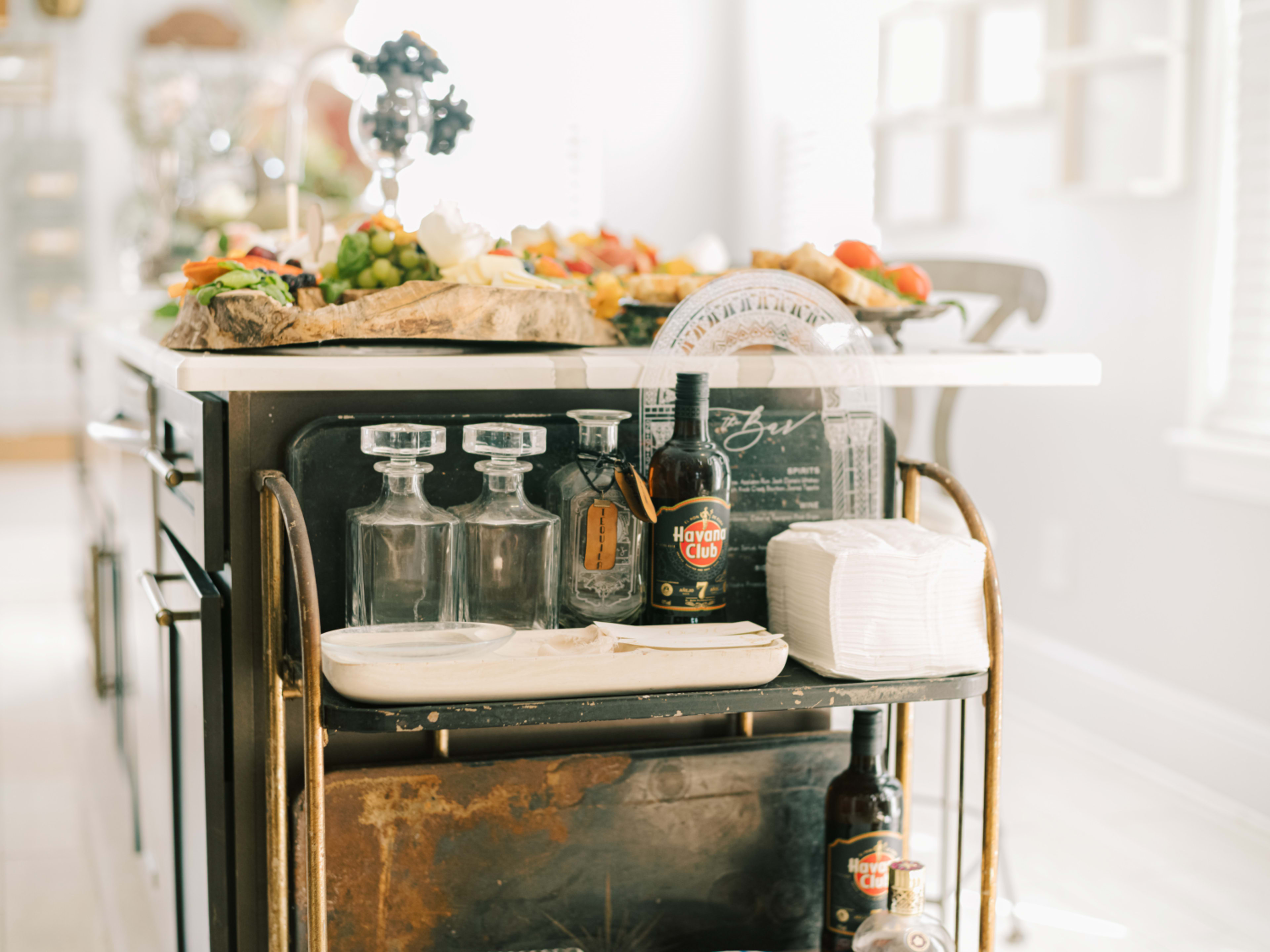 A kitchen island features a variety of colorful fruit, glassware, and bottles displayed on a serving cart.