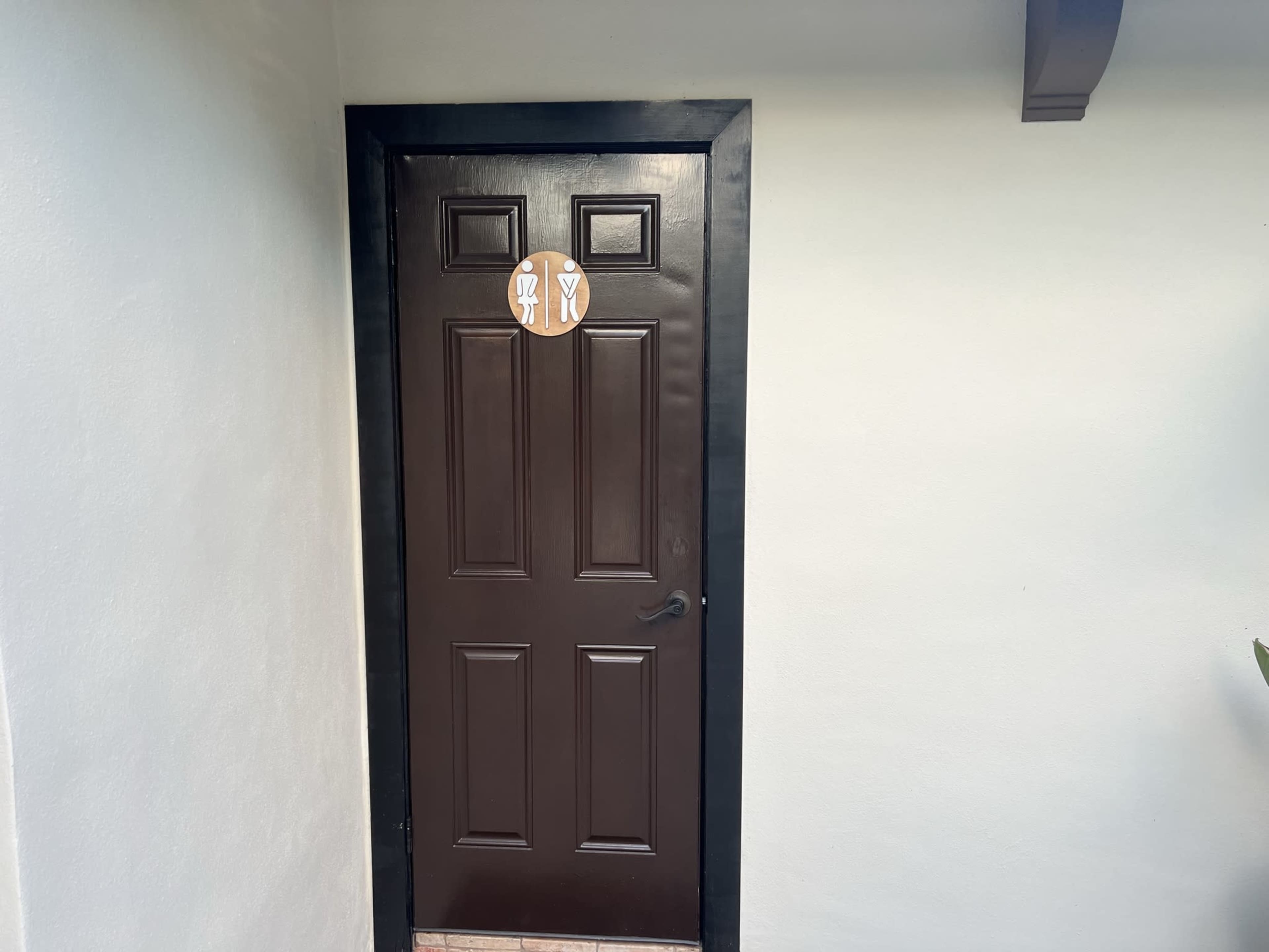A brown door with two circular signs depicting utensils, set against a white wall.