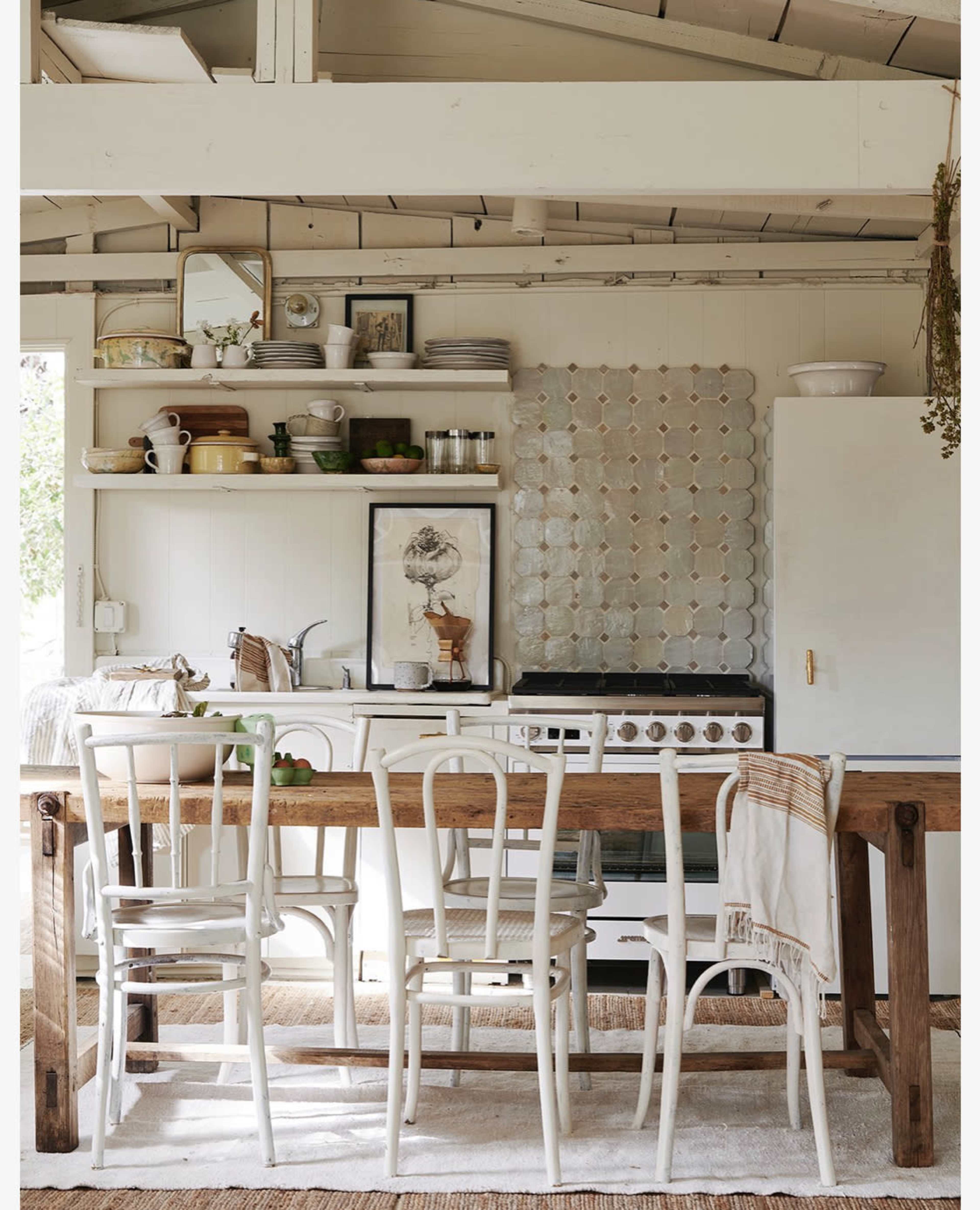 A rustic kitchen with wooden furniture, open shelving displaying kitchenware, and a gas stove against a white wall.