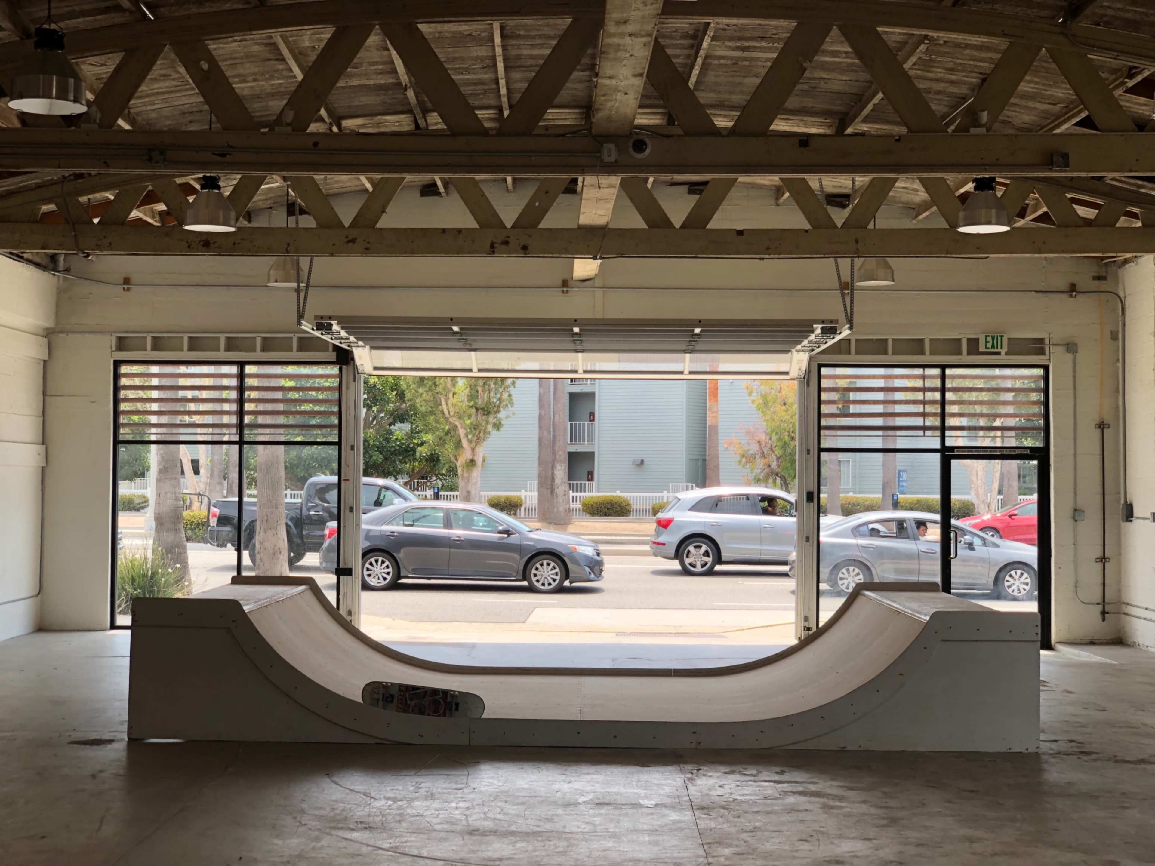 The image shows a skate ramp in an open indoor space with large windows and cars visible outside.