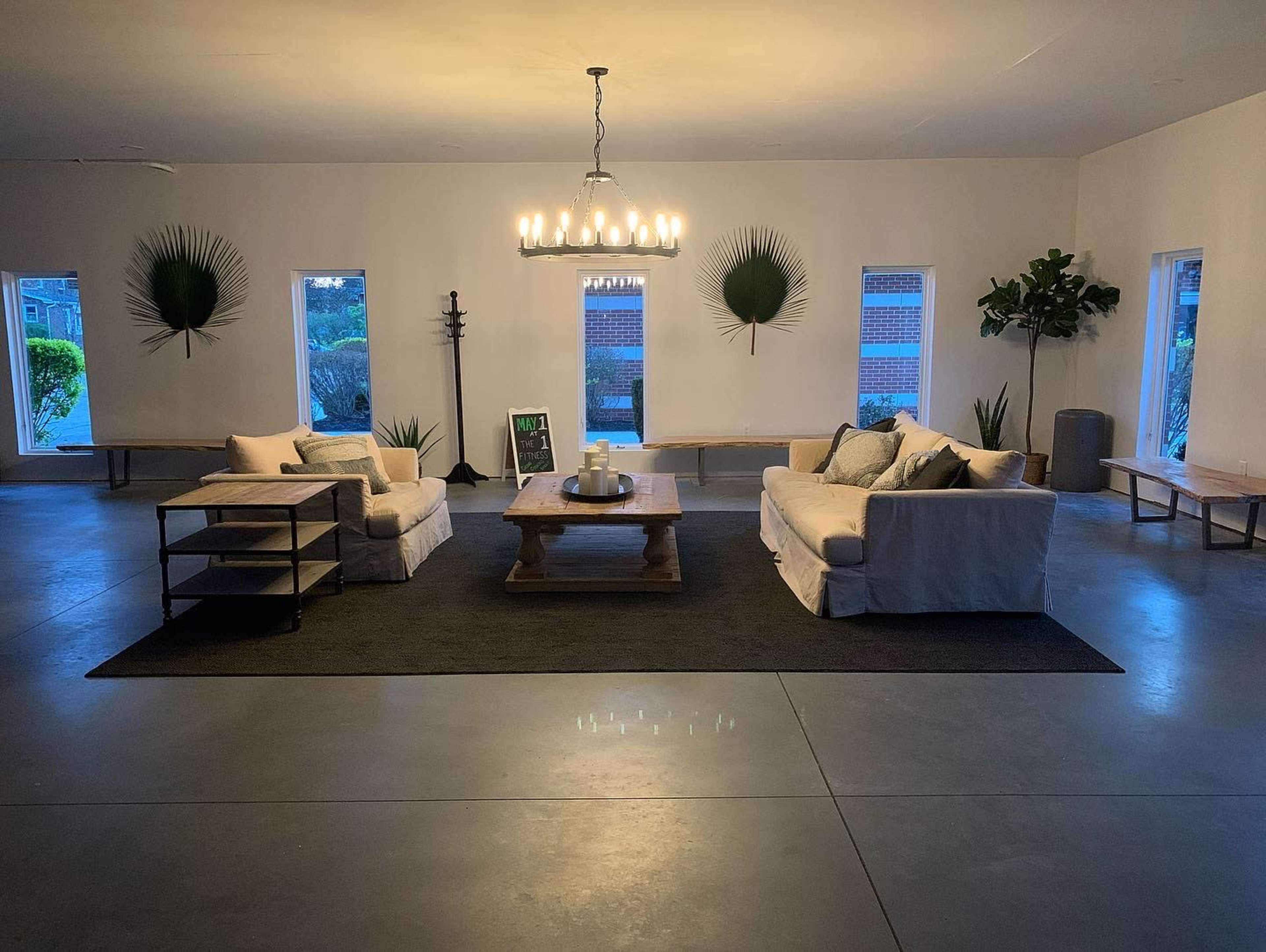 A spacious living room features two sofas facing a wooden table, with large windows and decorative plants accentuating the minimalist design.