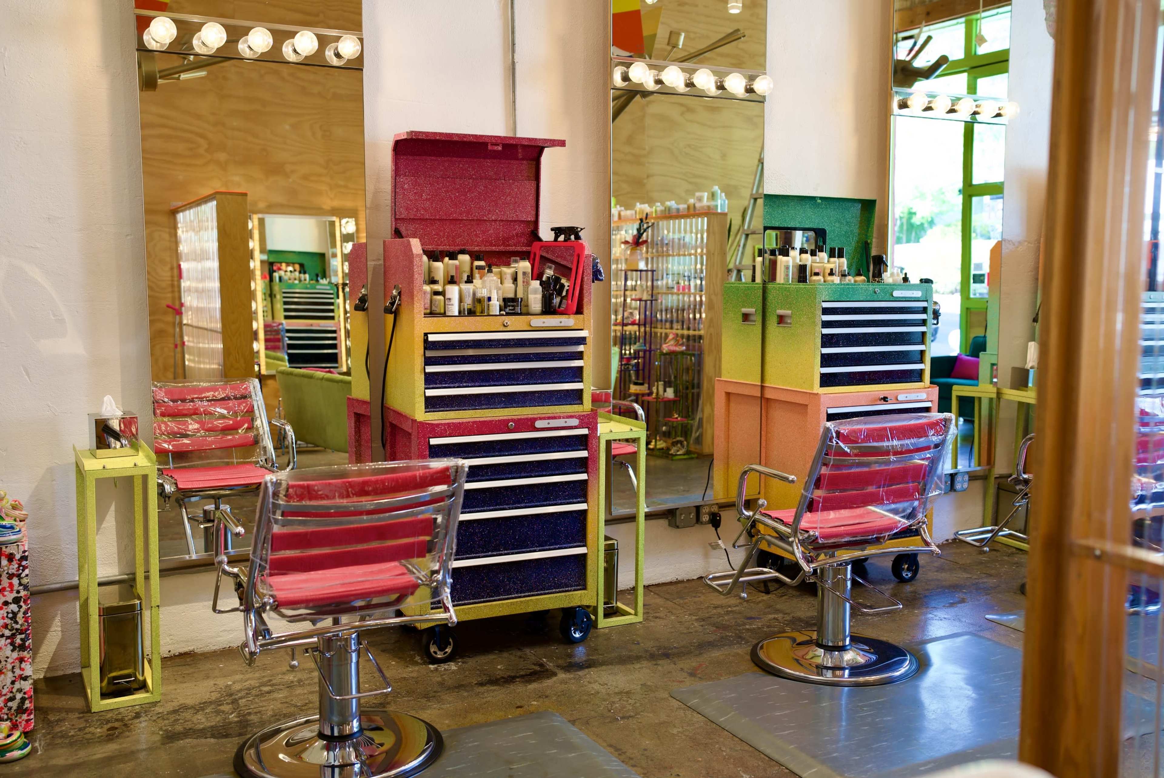 The image shows a brightly colored hair salon with two styling chairs and a rolling tool chest filled with hair products.