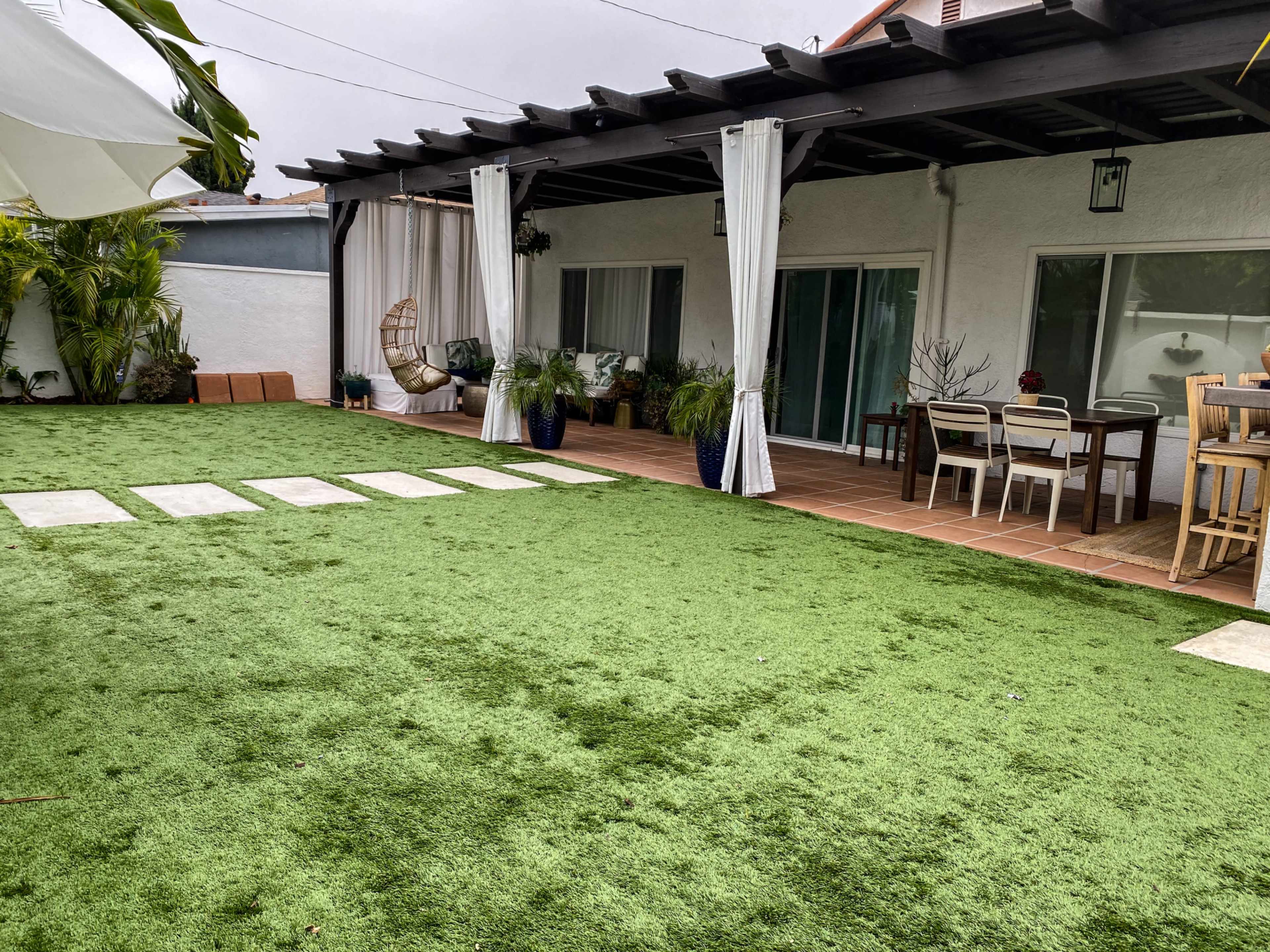 A spacious outdoor area with artificial grass, featuring a dining table, lounge chairs, and potted plants.