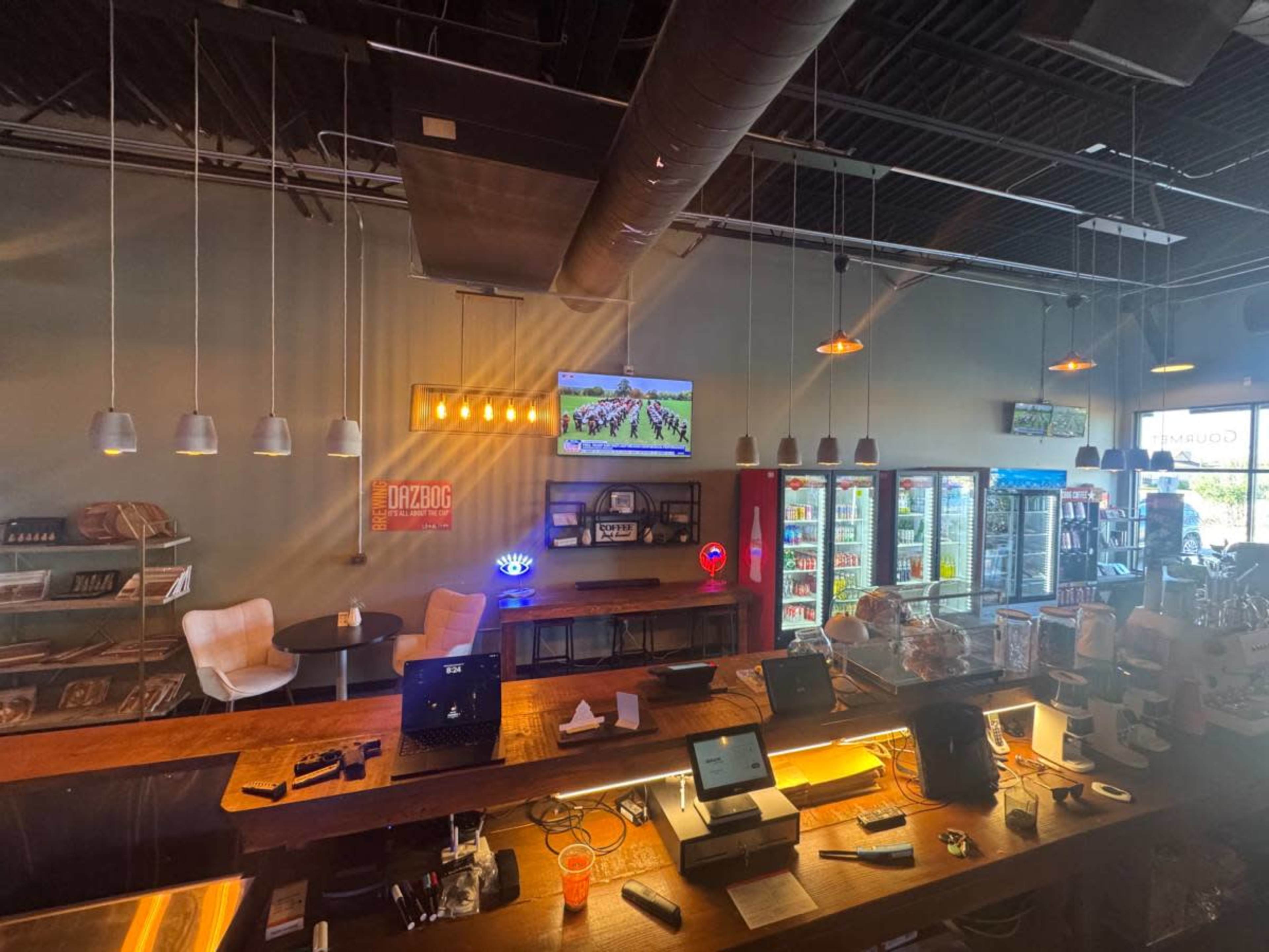 The image shows an indoor bar setting with a wooden counter, refrigerators in the background, and a TV displaying a sports game.