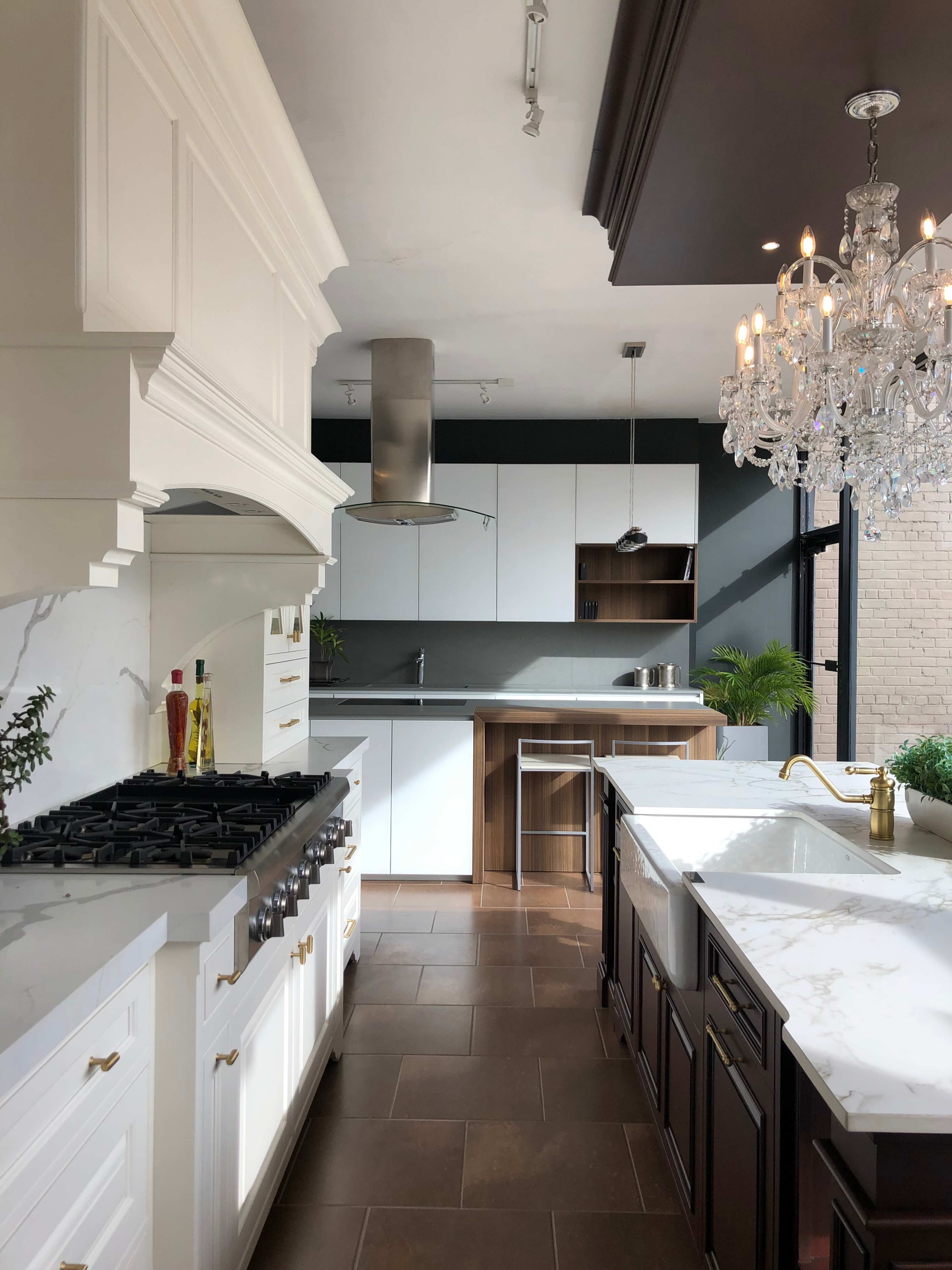 A modern kitchen features a combination of white cabinetry, a stainless steel range hood, dark countertops, and a large island with a marble surface.