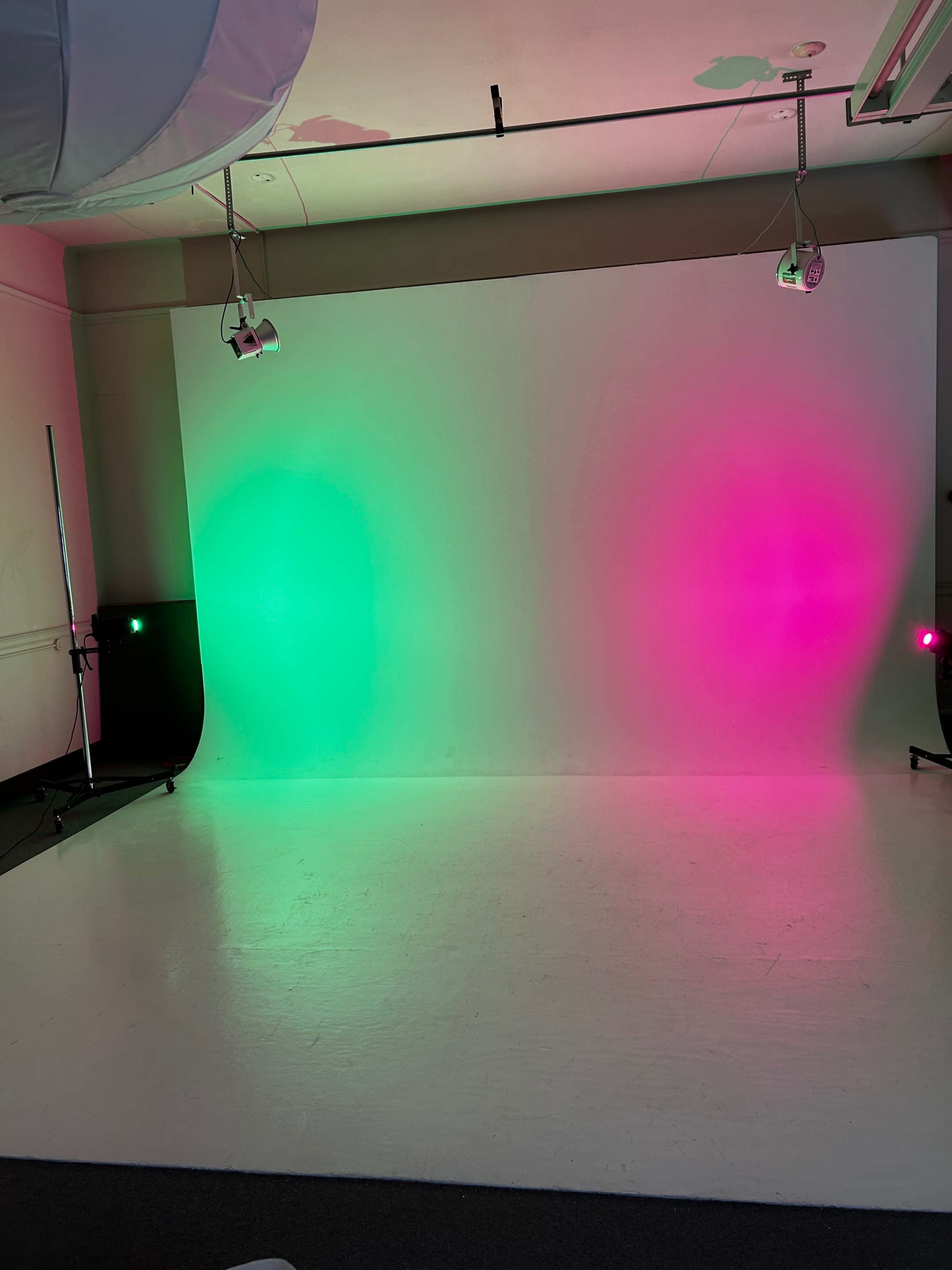 The image shows a photo studio with a blank backdrop illuminated by green and pink lights.