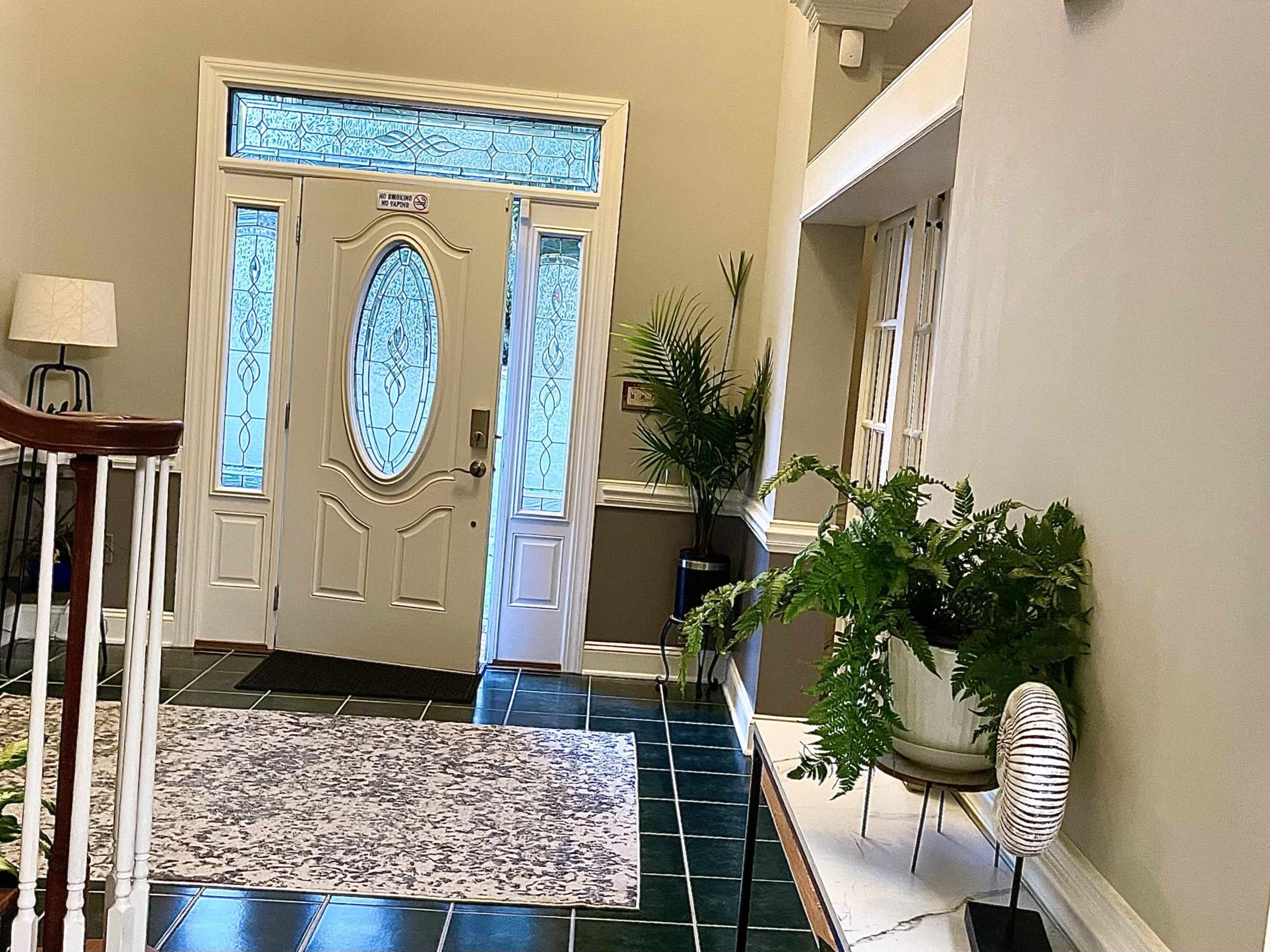 An interior entrance hall with a decorative rug, a doorway with stained glass, and a potted plant on the side.