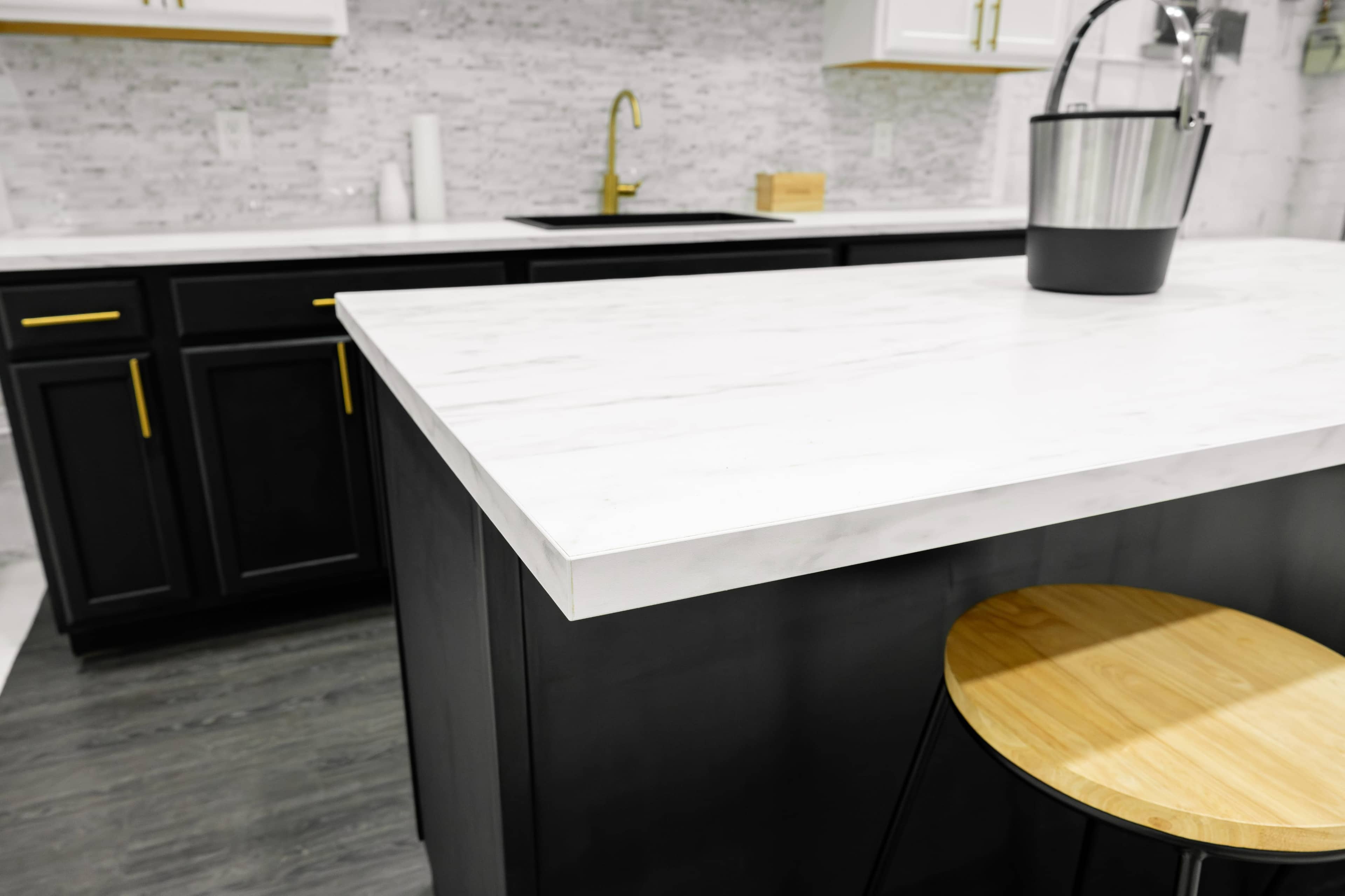 A modern kitchen features a marble countertop, black cabinetry, and a wooden bar stool.