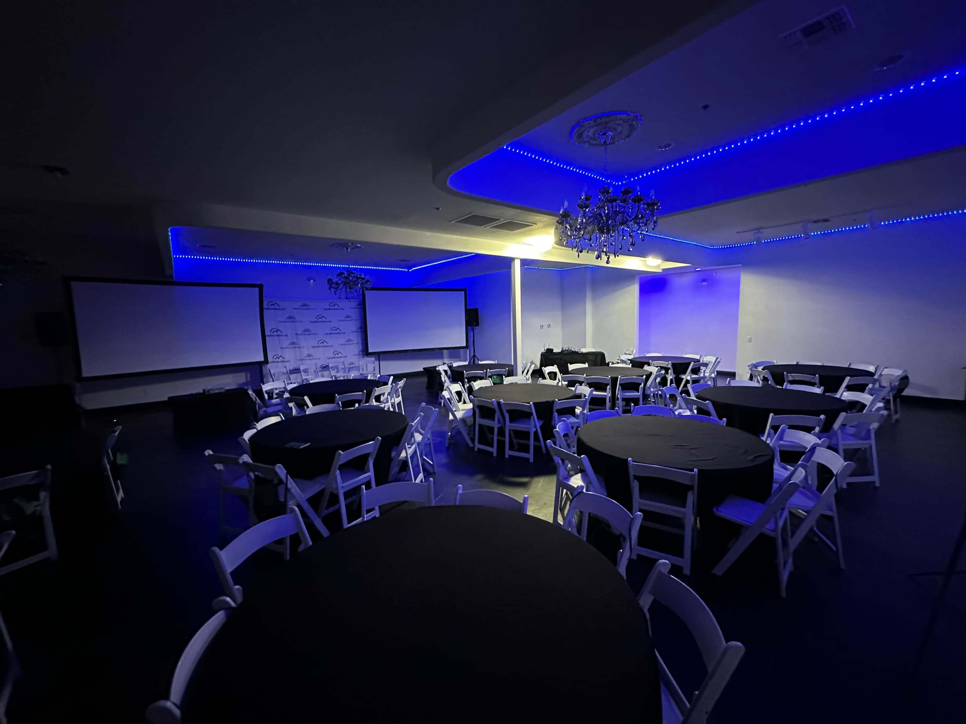 The image shows a spacious event room arranged with circular tables and chairs, illuminated by blue LED lights.