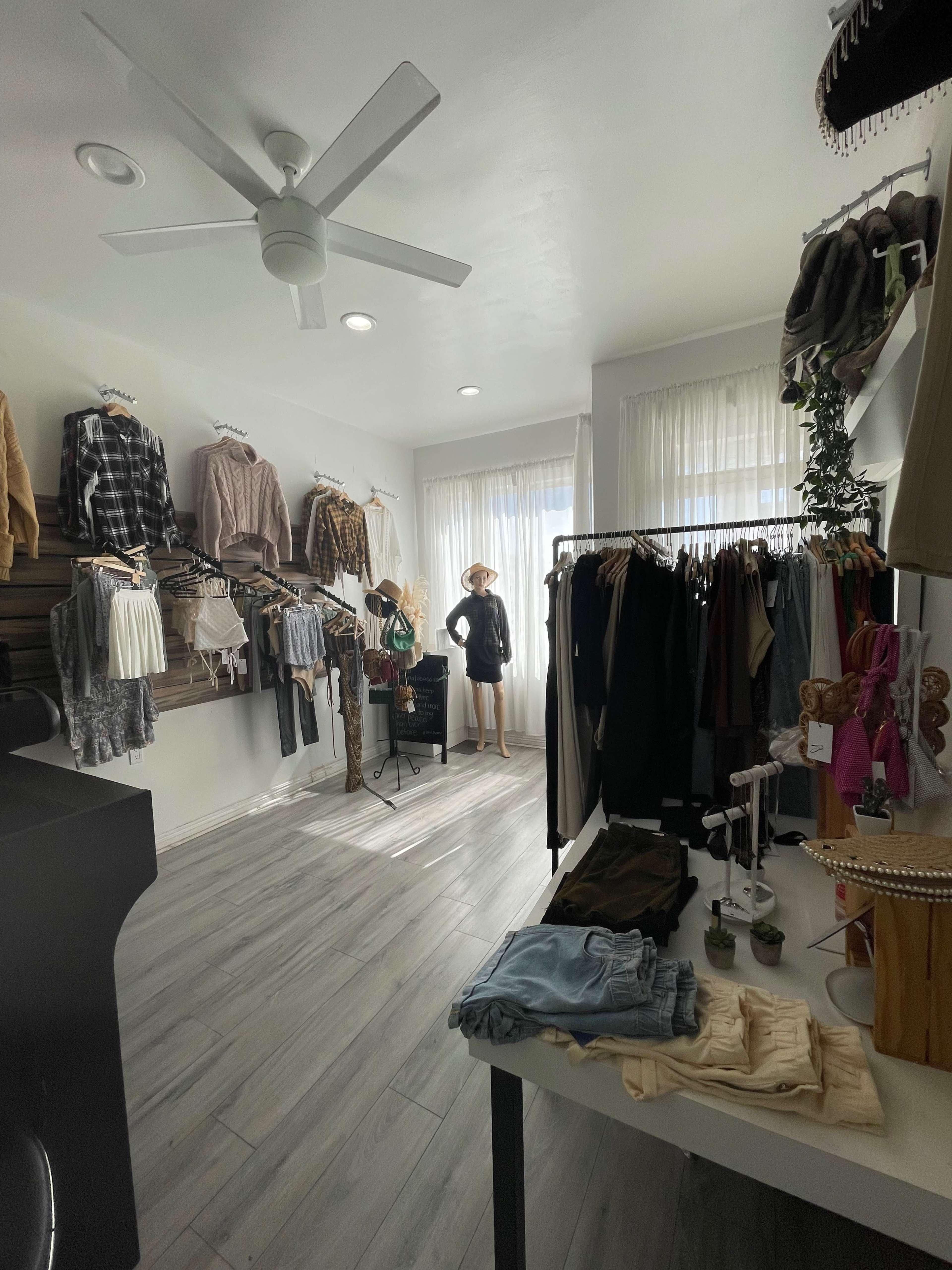 A clothing boutique with racks of apparel on the walls and a mannequin displayed in the center near a window.