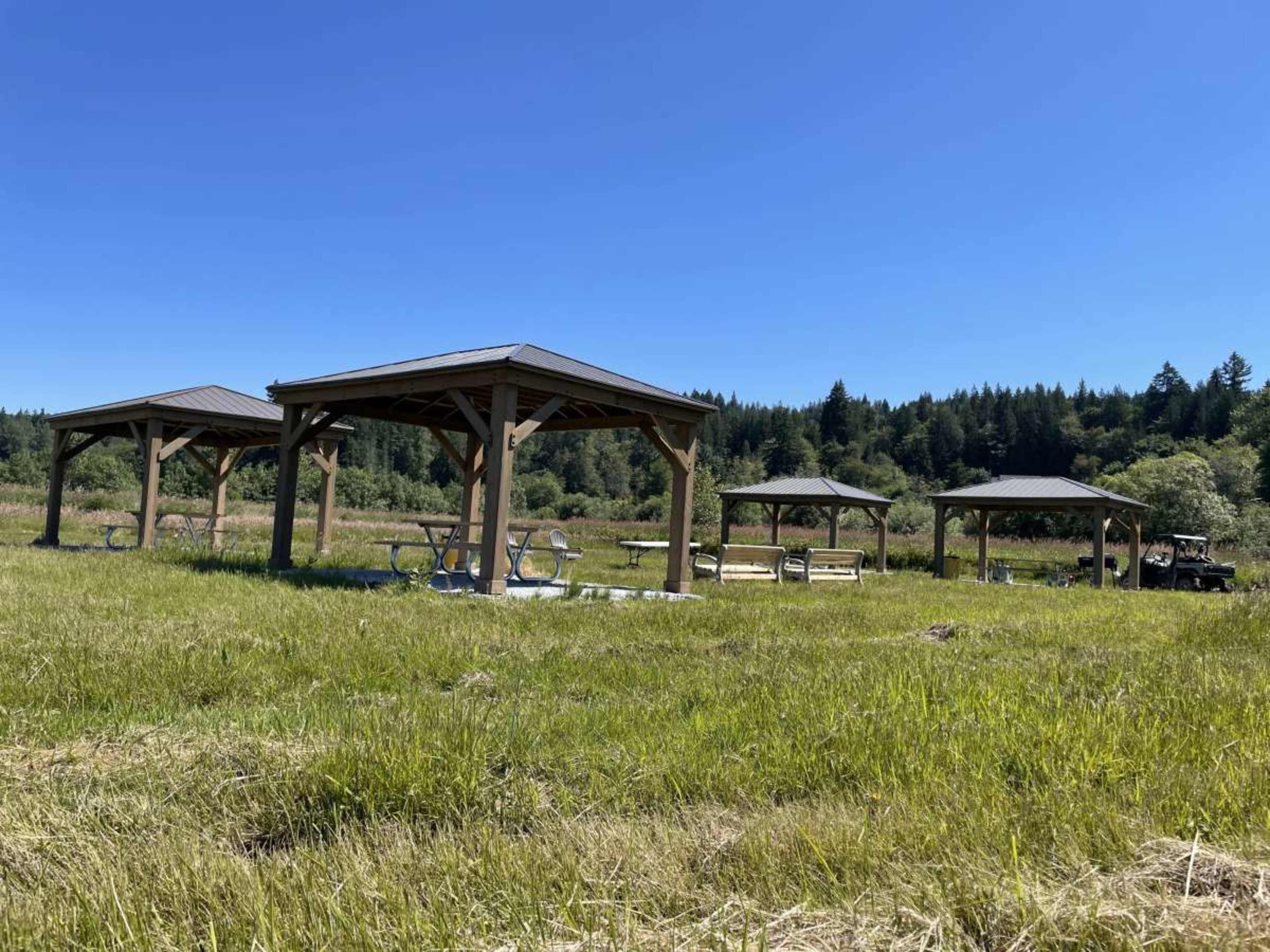 Several wooden pavilions set up in a grassy field under a clear blue sky.