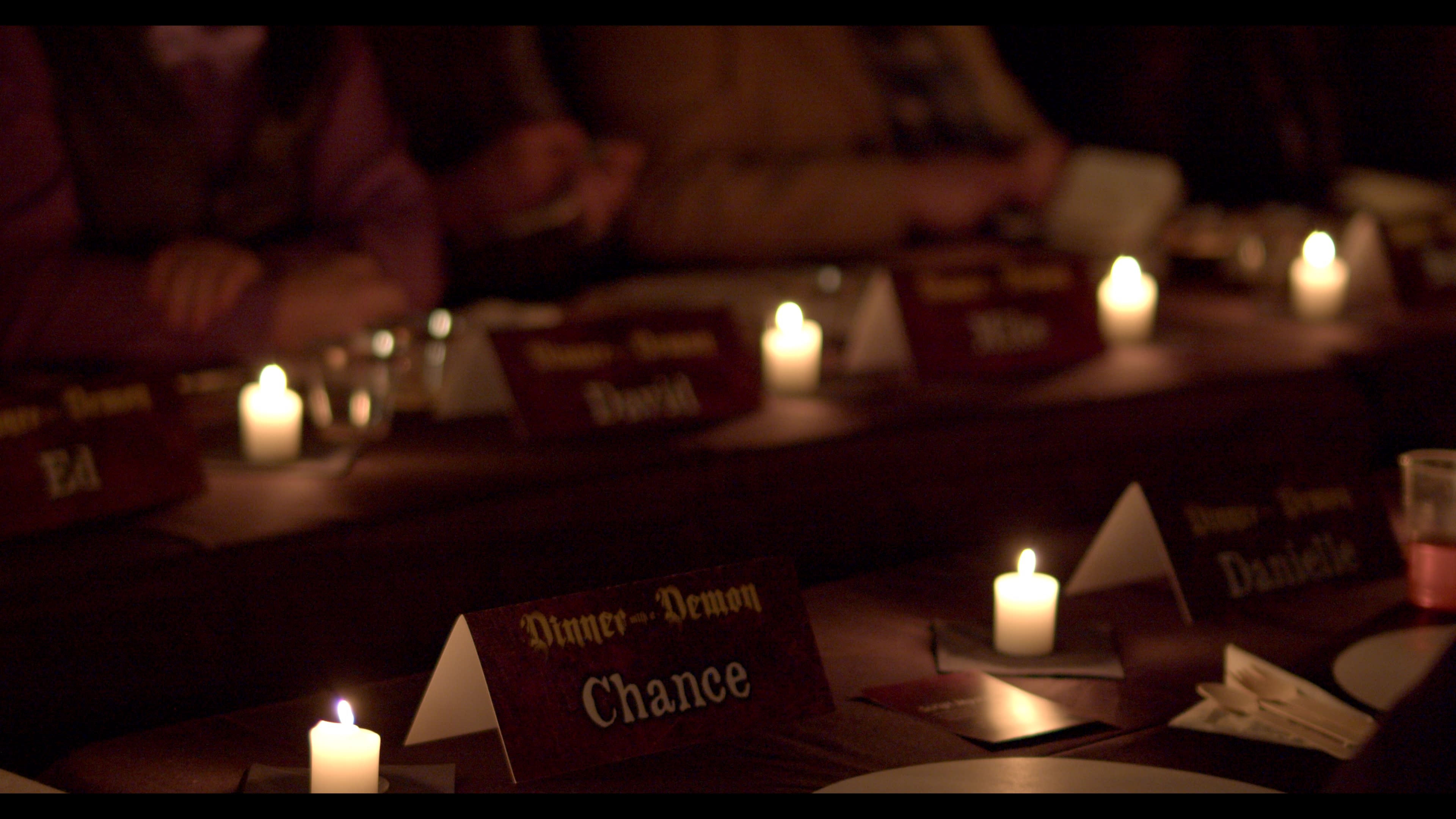A dimly lit dining setting features several nameplates on a table, with flickering candles creating a warm ambiance.
