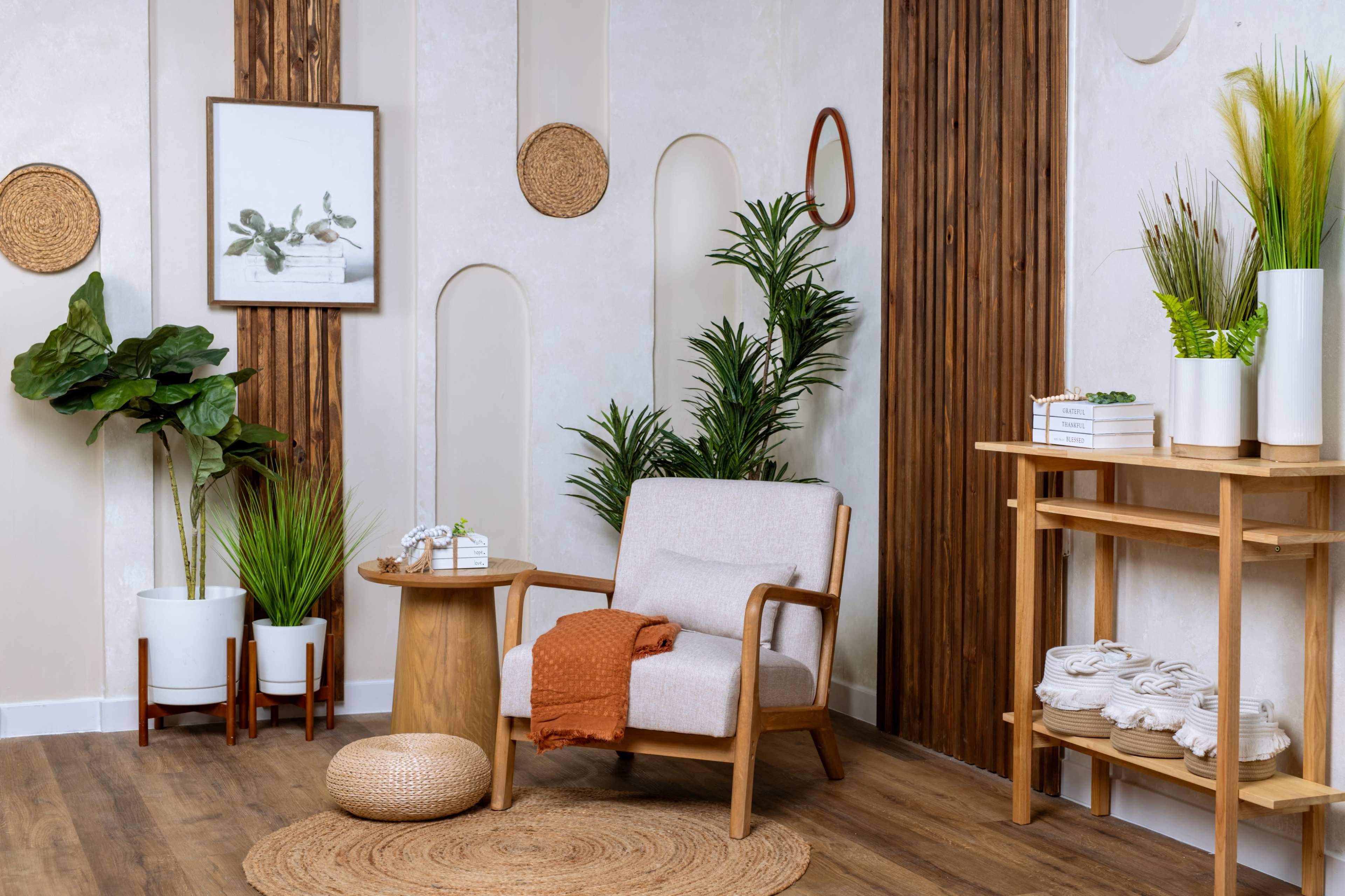 A cozy living space with a light-colored armchair, a circular table, decorative plants, and a wooden shelf displaying towels and a framed artwork on the wall.