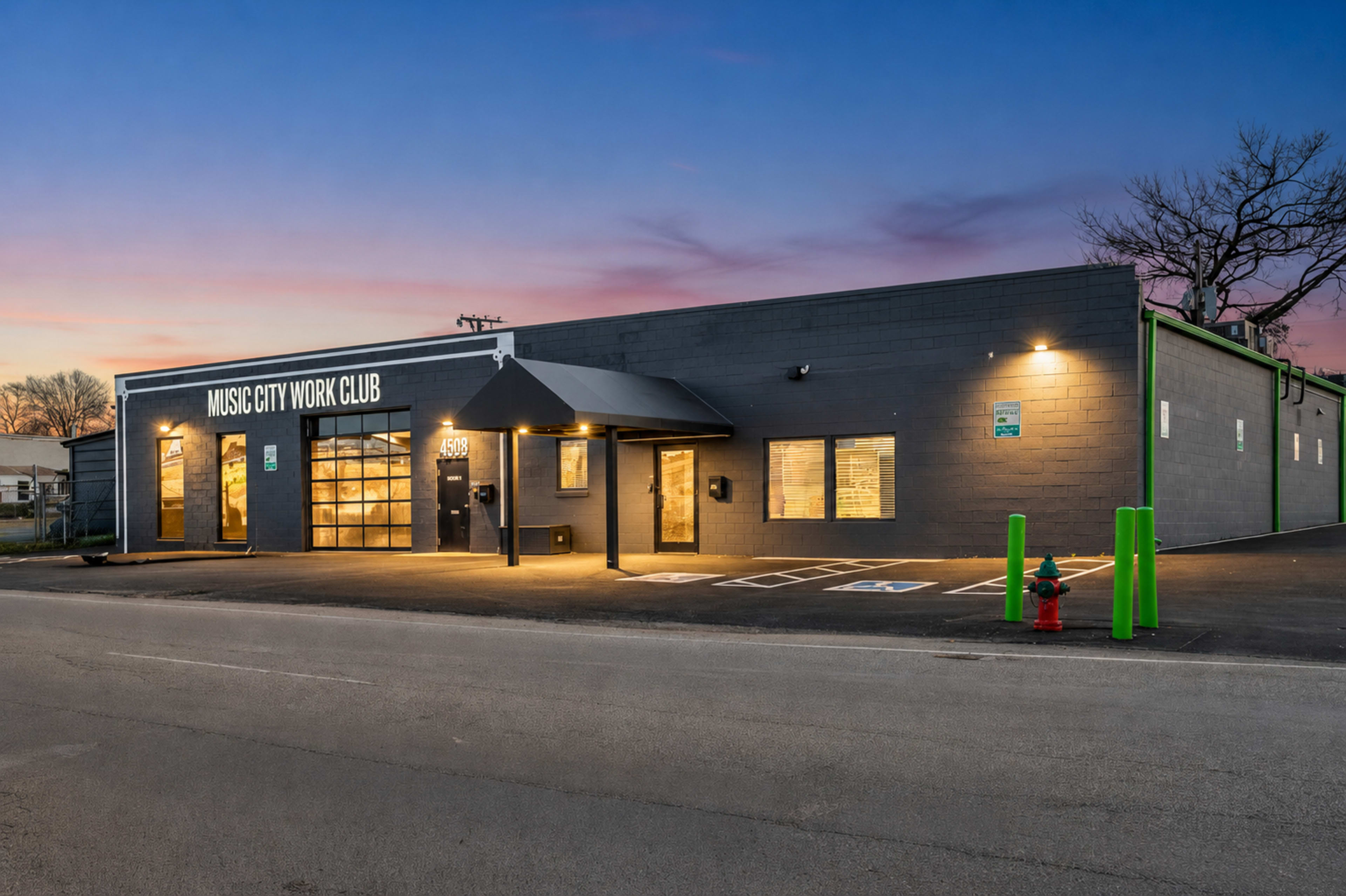 The image shows a modern building with a black exterior and a covered entrance, labeled "Music City Work Club," situated next to a road at dusk.