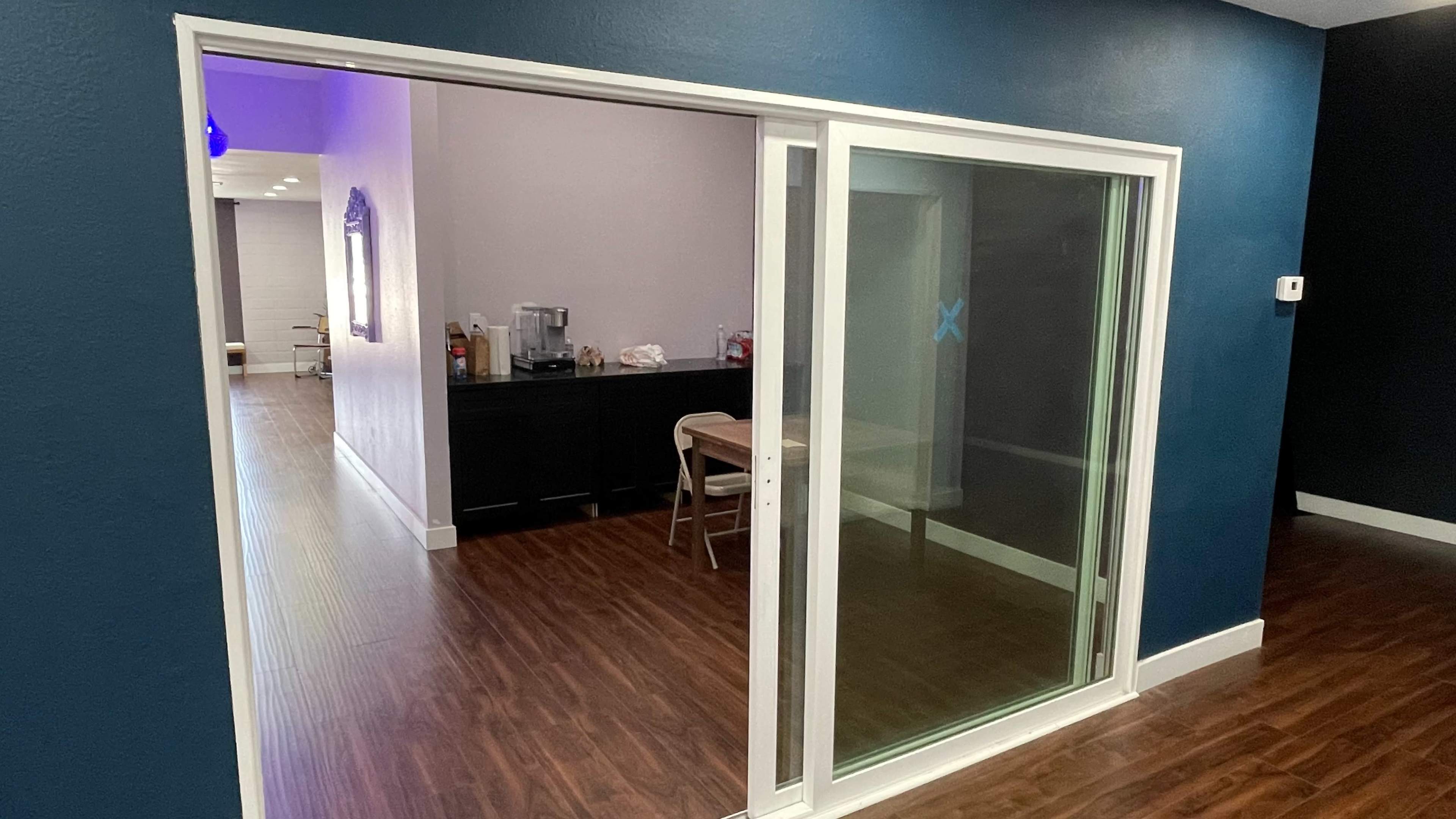 A glass door leading from a dark teal wall into a room with light-colored walls and wooden flooring.