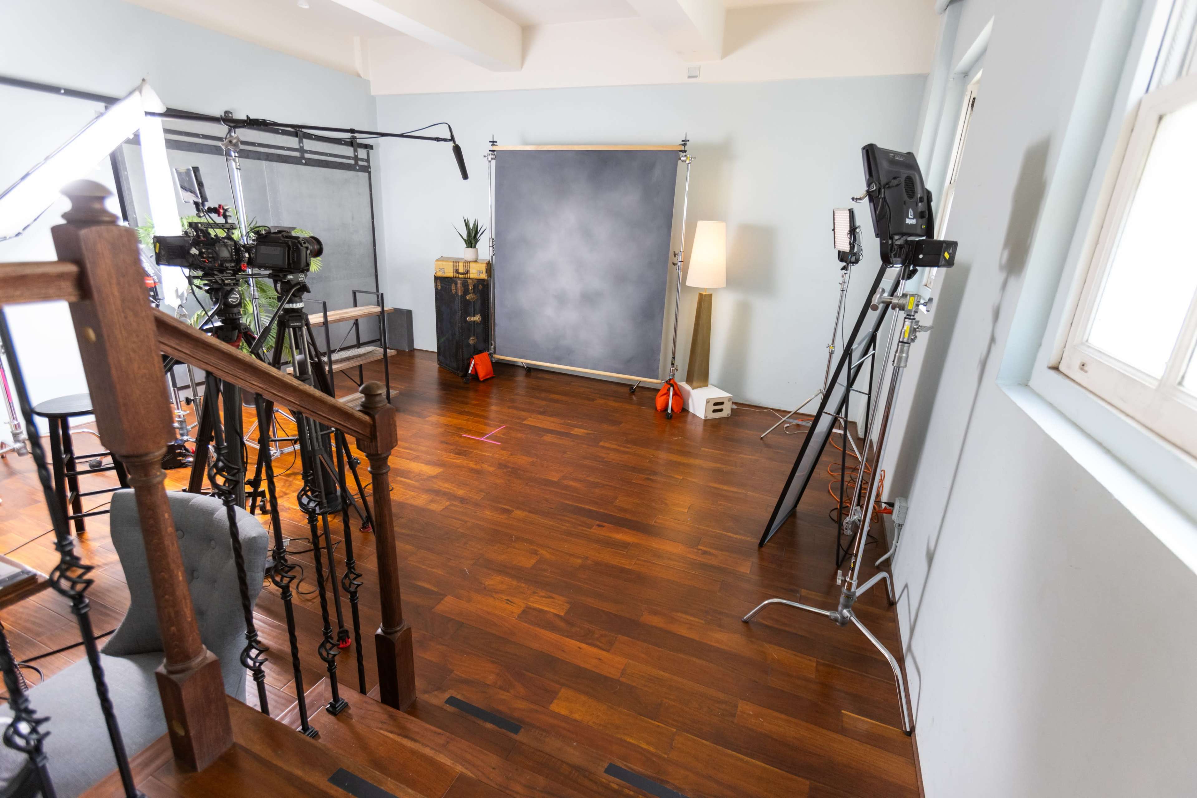 A photography or filming studio is set up with various equipment, including cameras, lighting, and a backdrop, all arranged on polished wooden flooring.