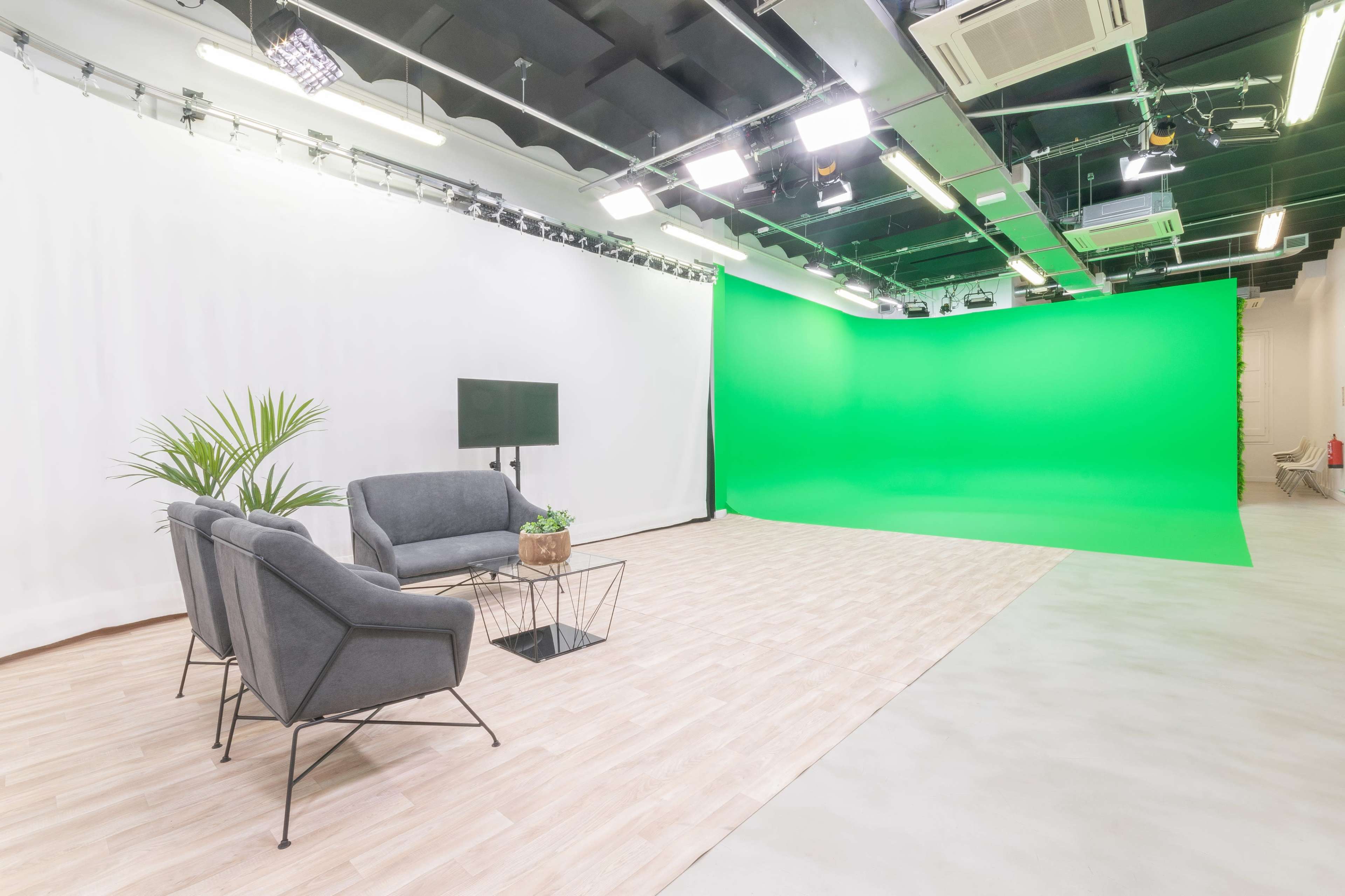 A clean studio space features a gray sofa and chair set against a green screen backdrop and white curtains.