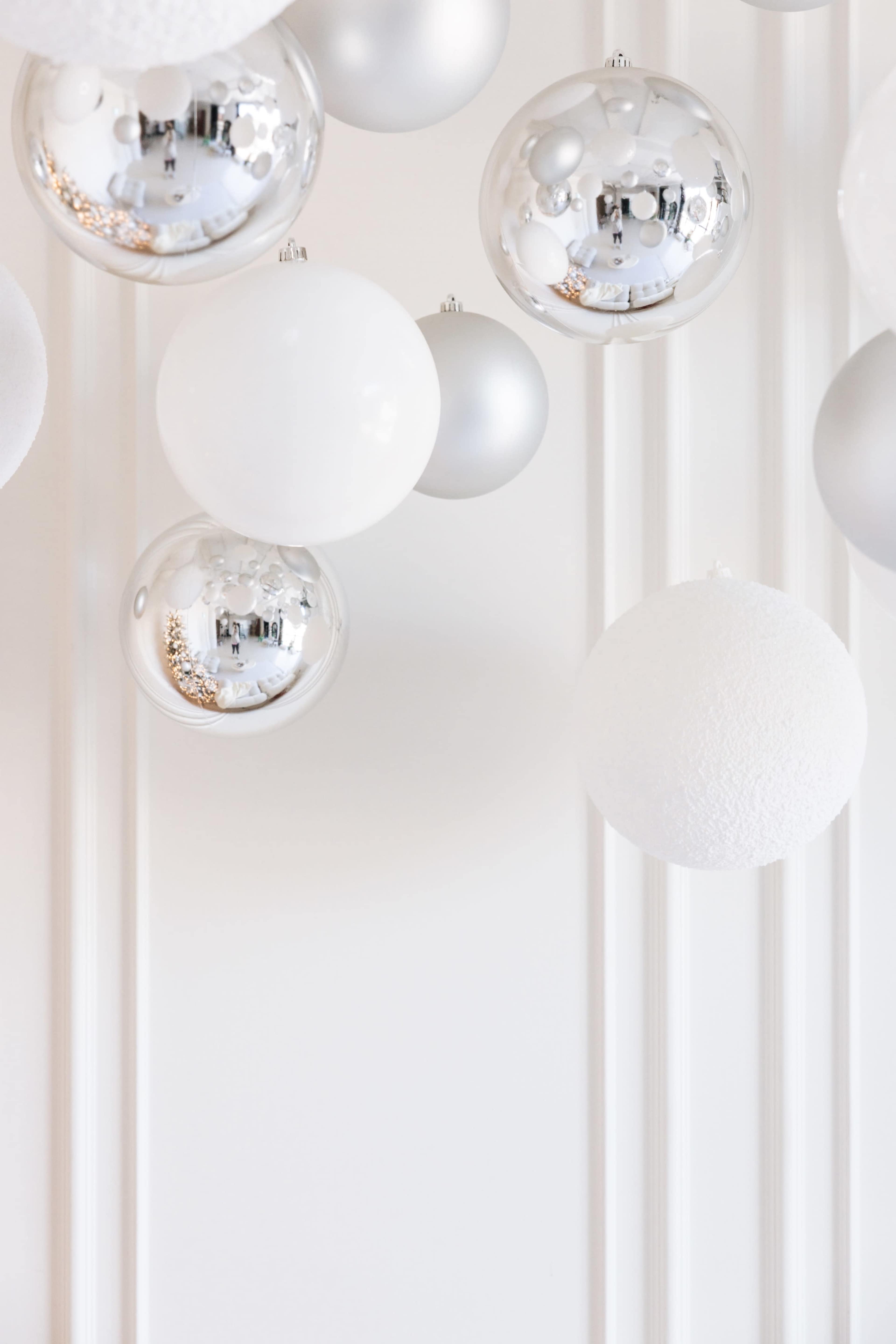 The image features a variety of silver and white decorative baubles hanging against a light-colored wall.