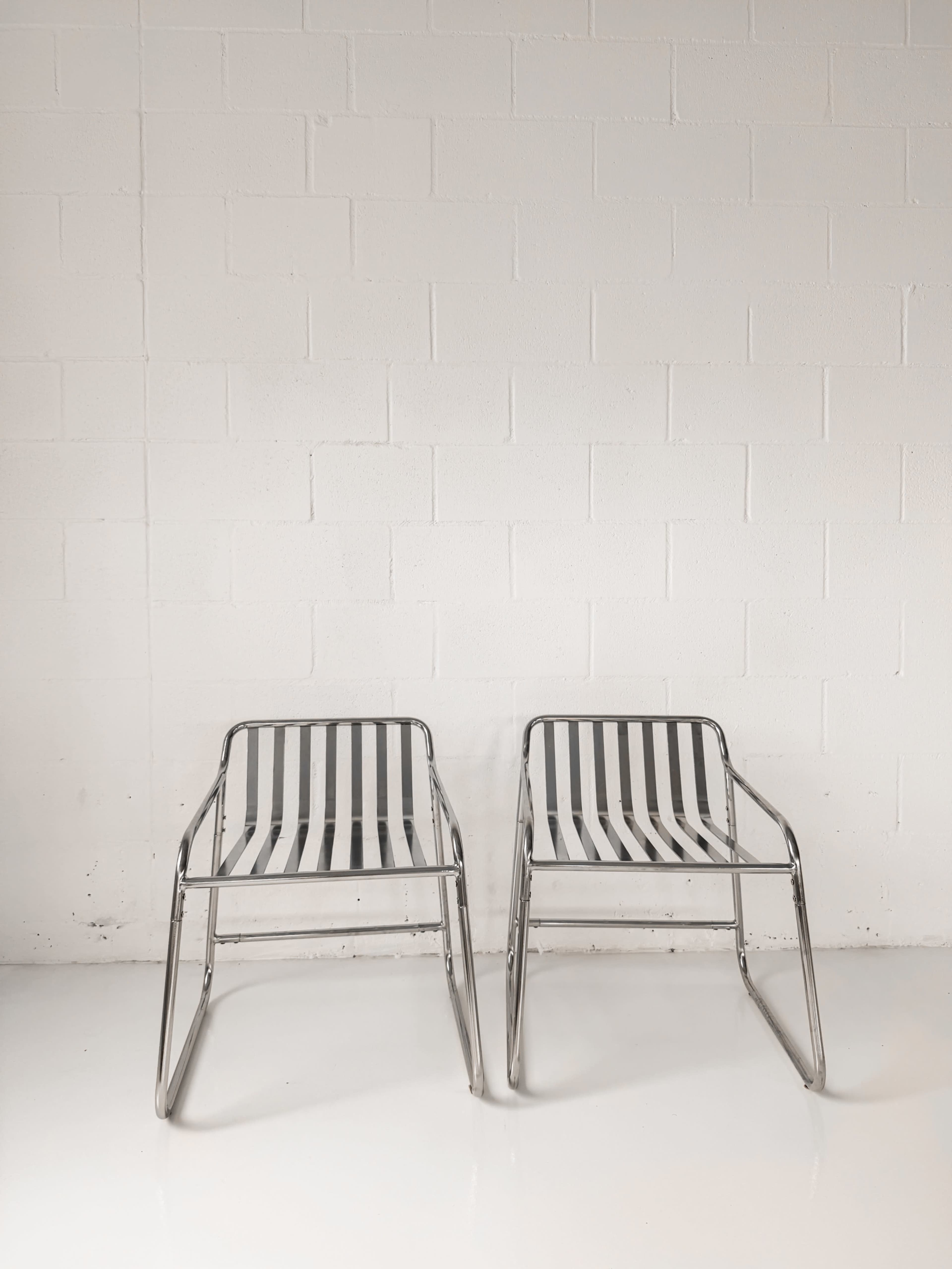 Two metal-framed chairs with striped fabric seats are positioned facing each other against a white wall.