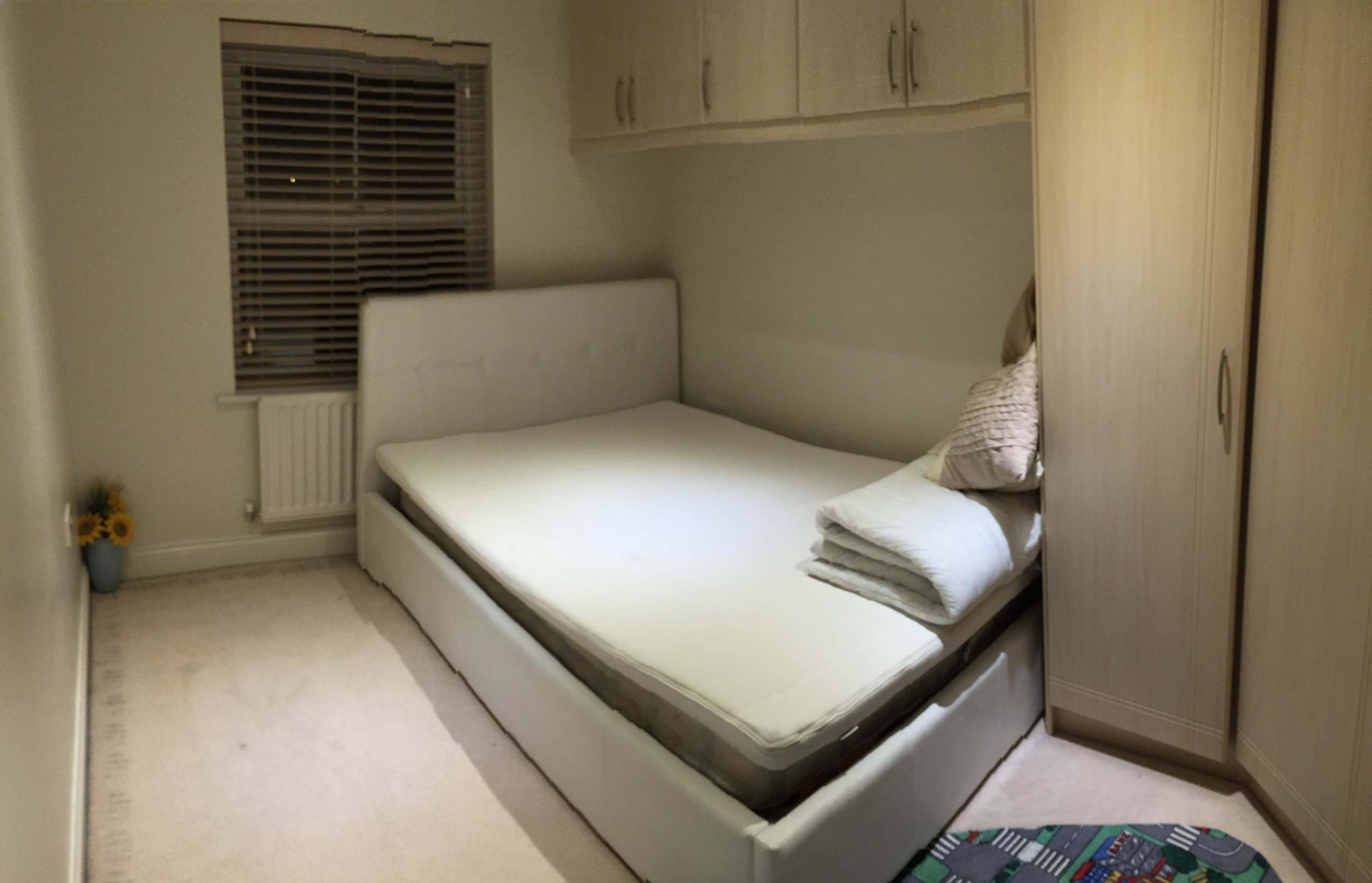 A bedroom with a bed frame and a plain mattress positioned against a wall, accompanied by a folded blanket and a few decorative items.