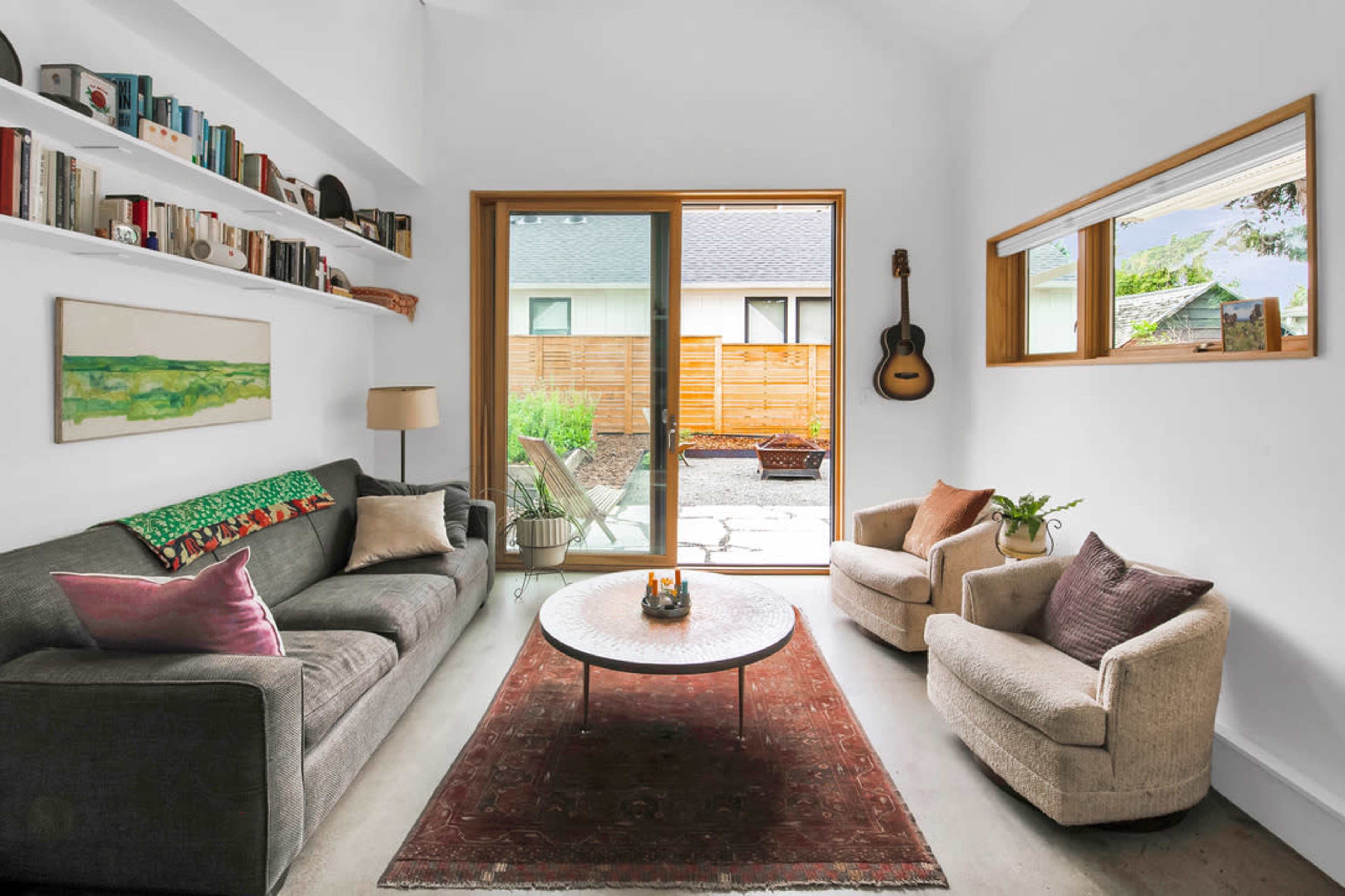 A modern living room with a gray sofa, two armchairs, a round coffee table, and large windows that open to a courtyard.