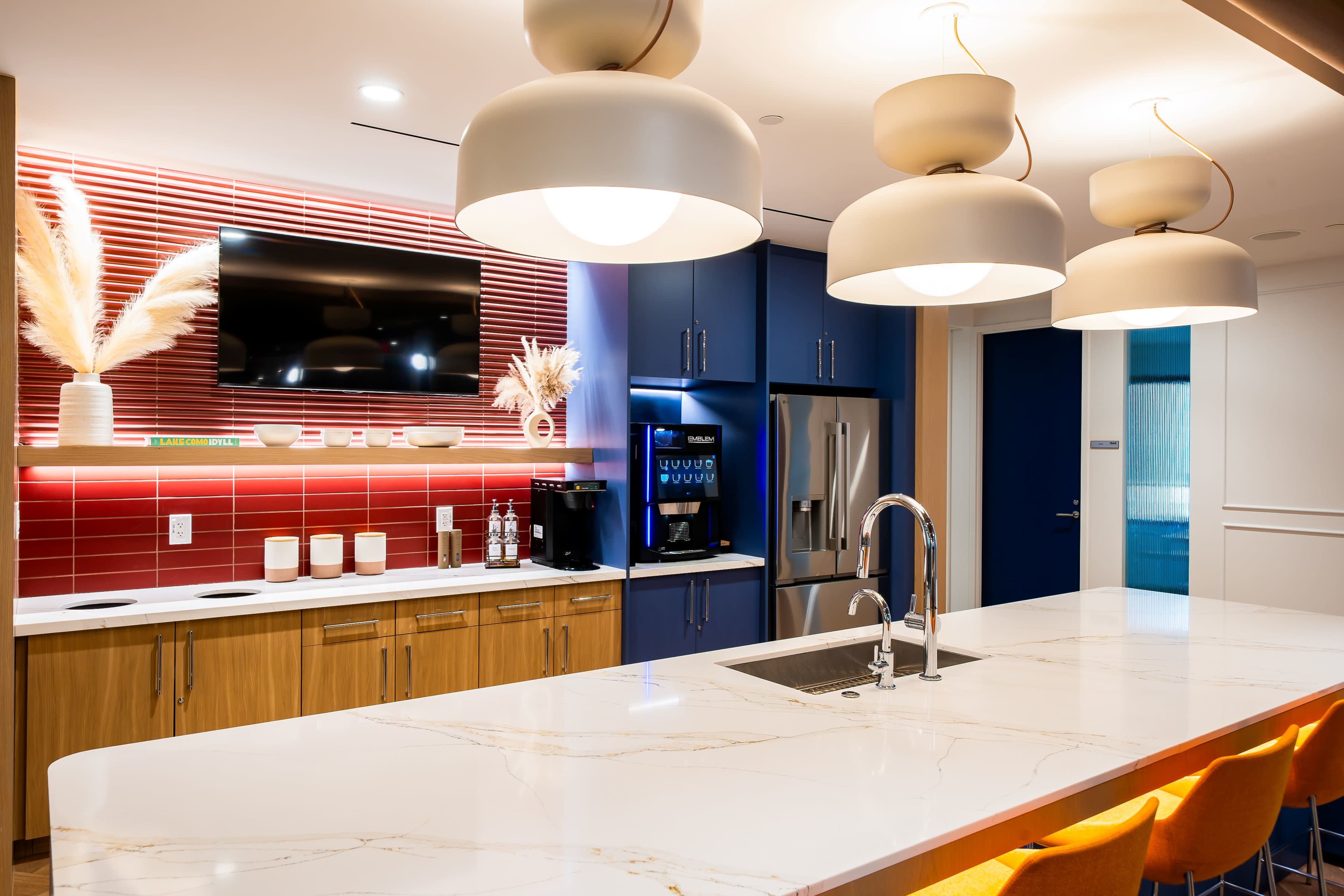 The kitchen features a large island with a marble countertop, modern appliances, and pendant lighting above, set against a backdrop of blue cabinetry and a red accent wall.