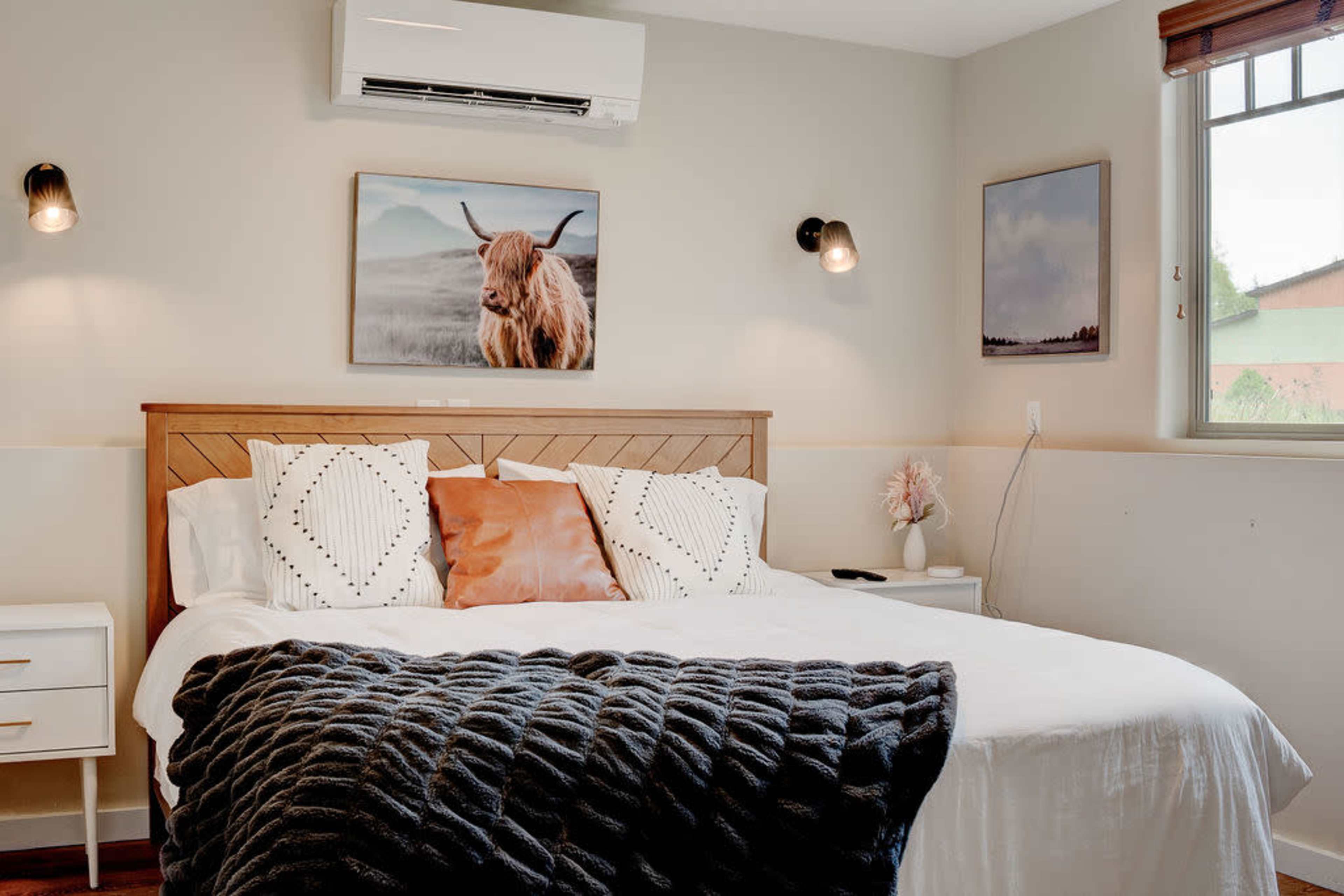 A neatly arranged bedroom with a queen-sized bed, two wall-mounted lights, and framed artwork above the headboard.