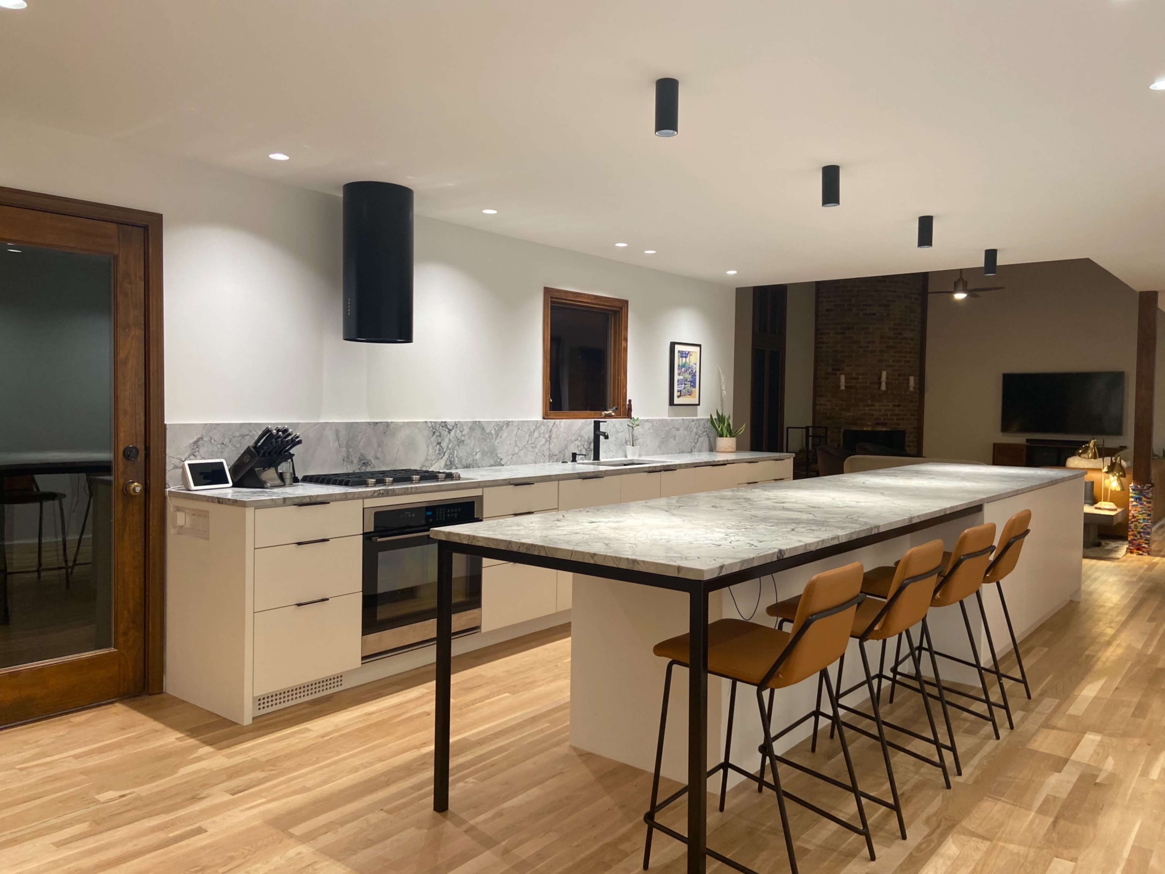 The image shows a modern kitchen featuring a large island with bar stools, sleek cabinetry, and a marble countertop, all illuminated by recessed lighting.